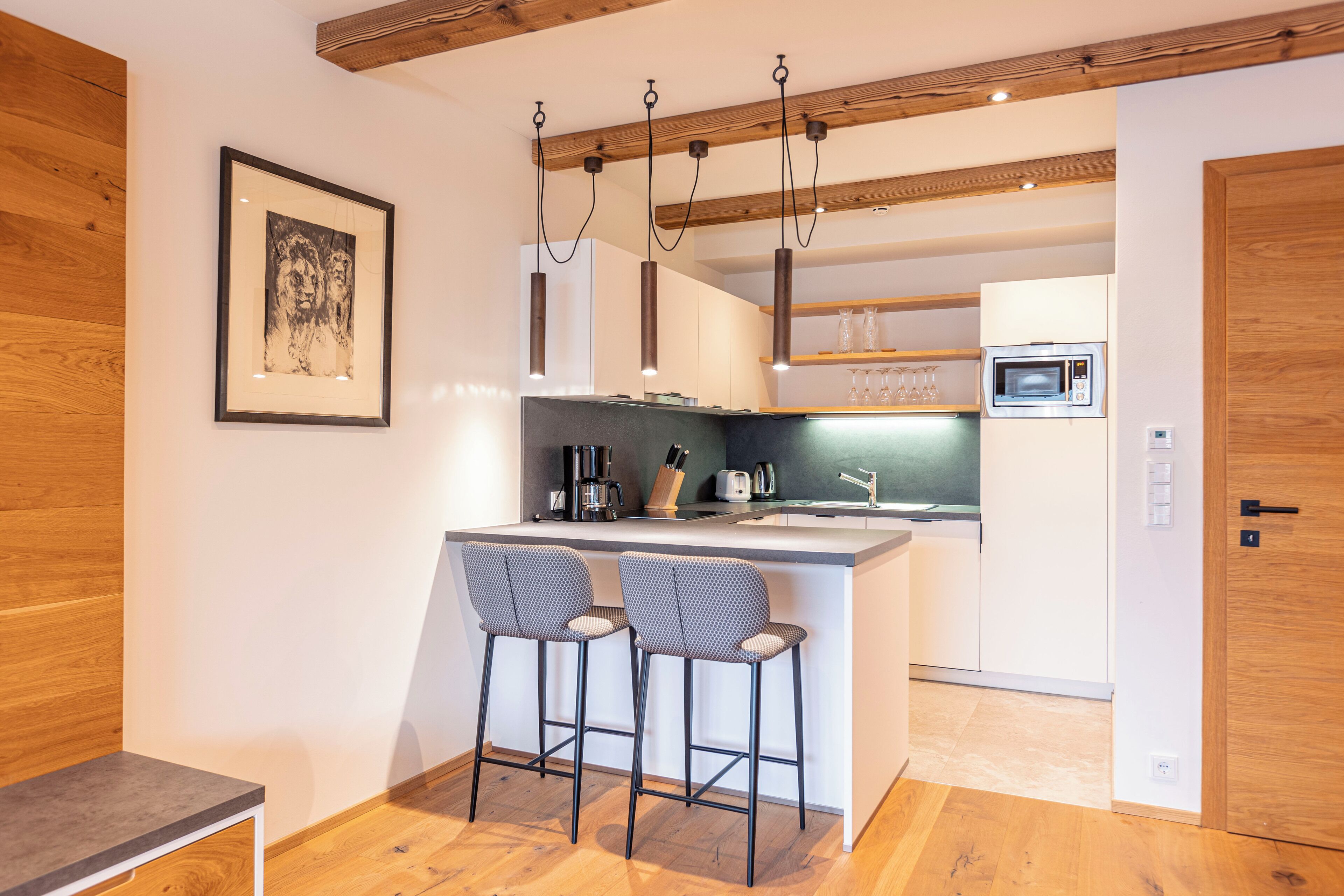 A modern kitchen with a bar area, wooden beams, and a framed artwork on the wall.