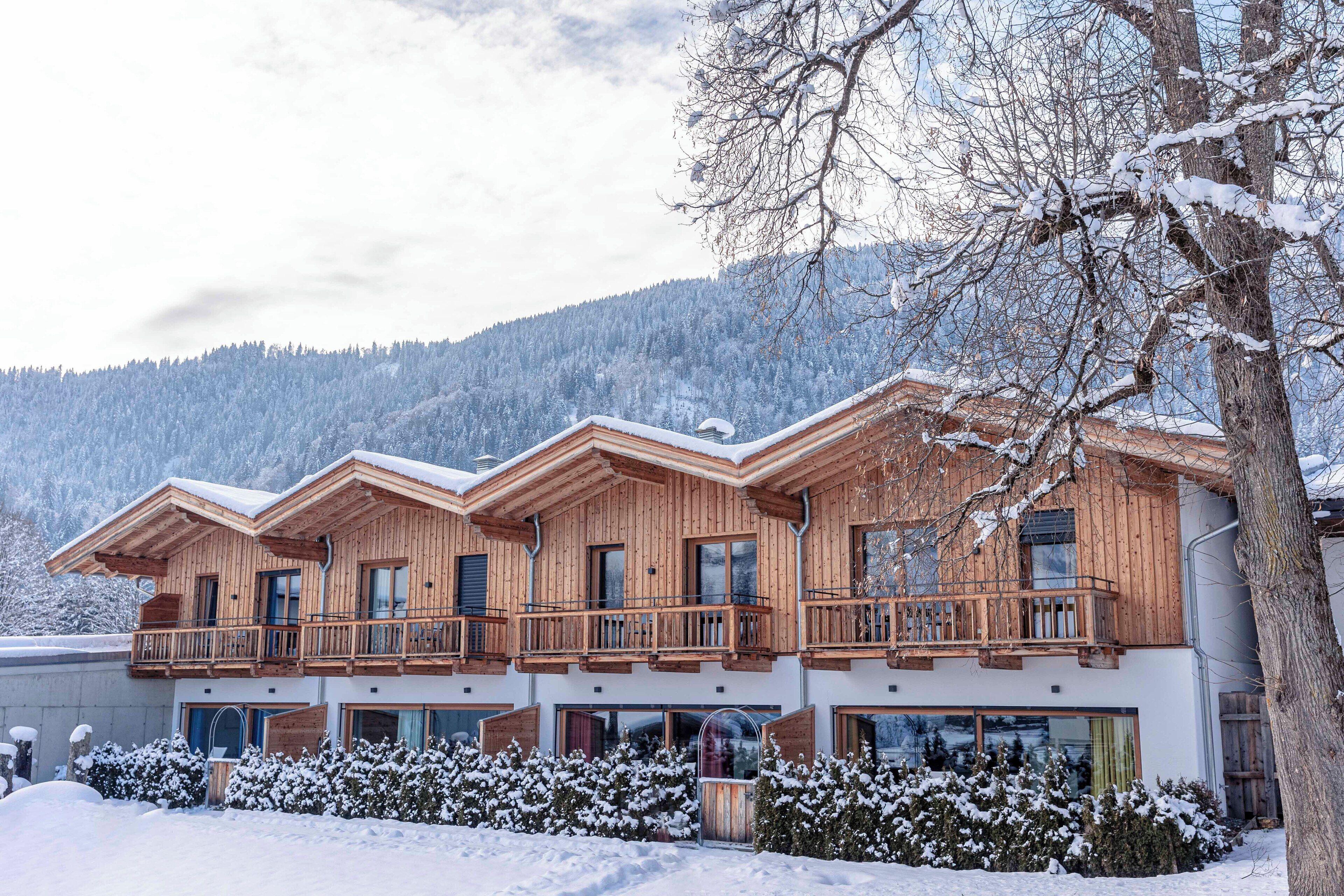 Ein mehrstöckiges Holzchalet mit Balkonen, großen Fenstern und einem verschneiten Berggrund.