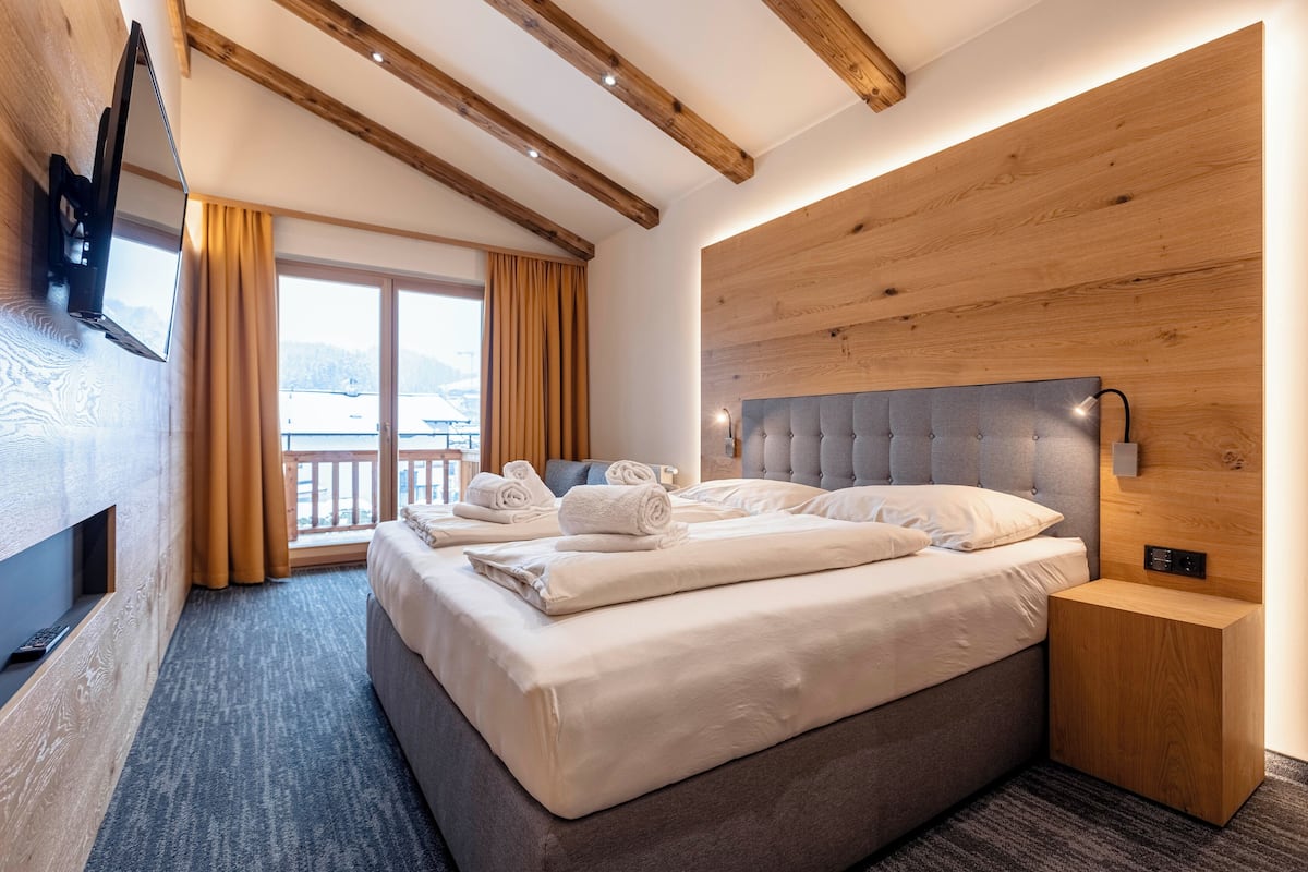 A modern hotel room with a large bed, a TV mounted on the wall, and a wooden headboard.