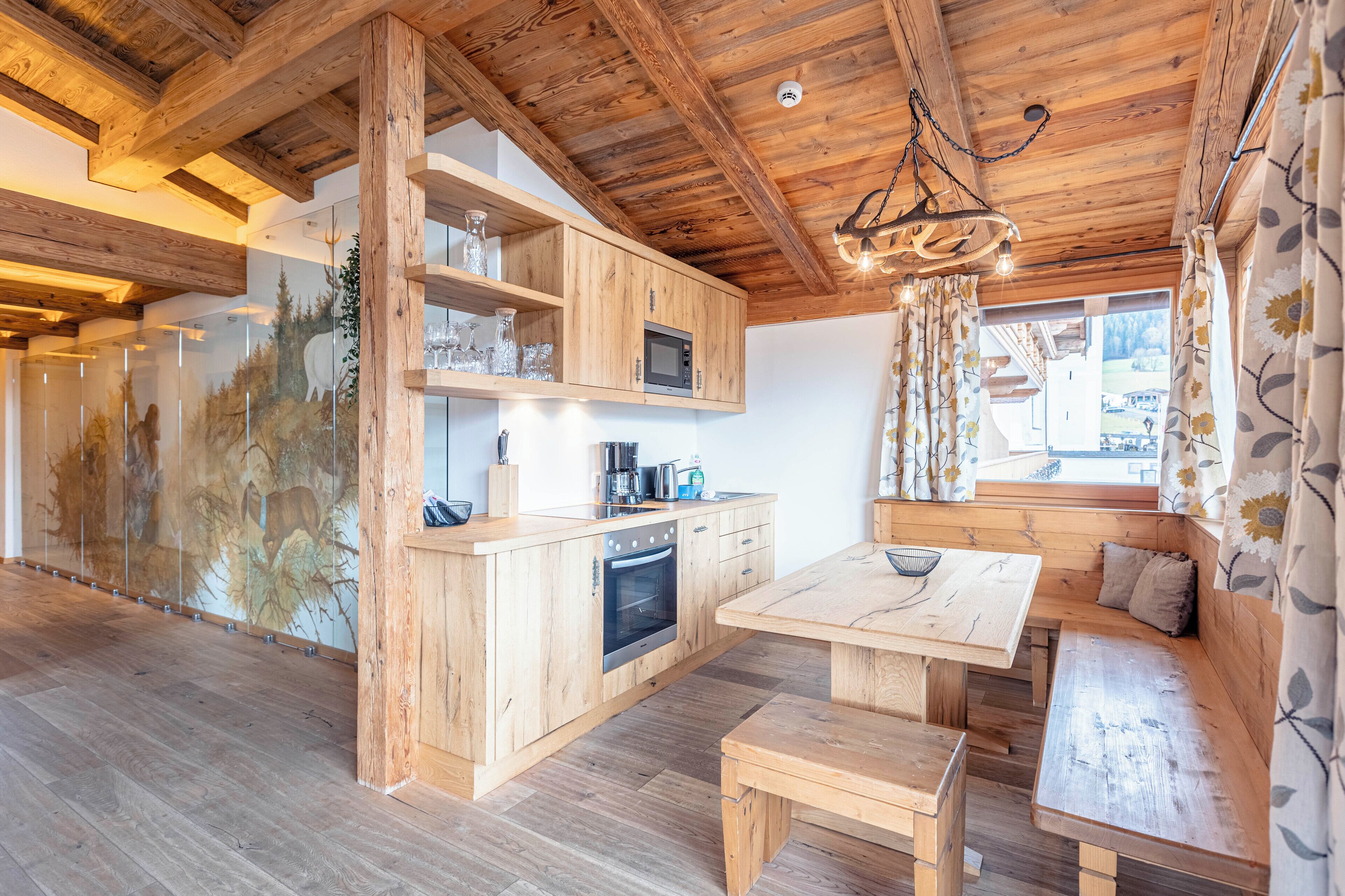 Een houten interieur met een keukenhoek, houten bankzitplaatsen en een uitzicht door een raam.