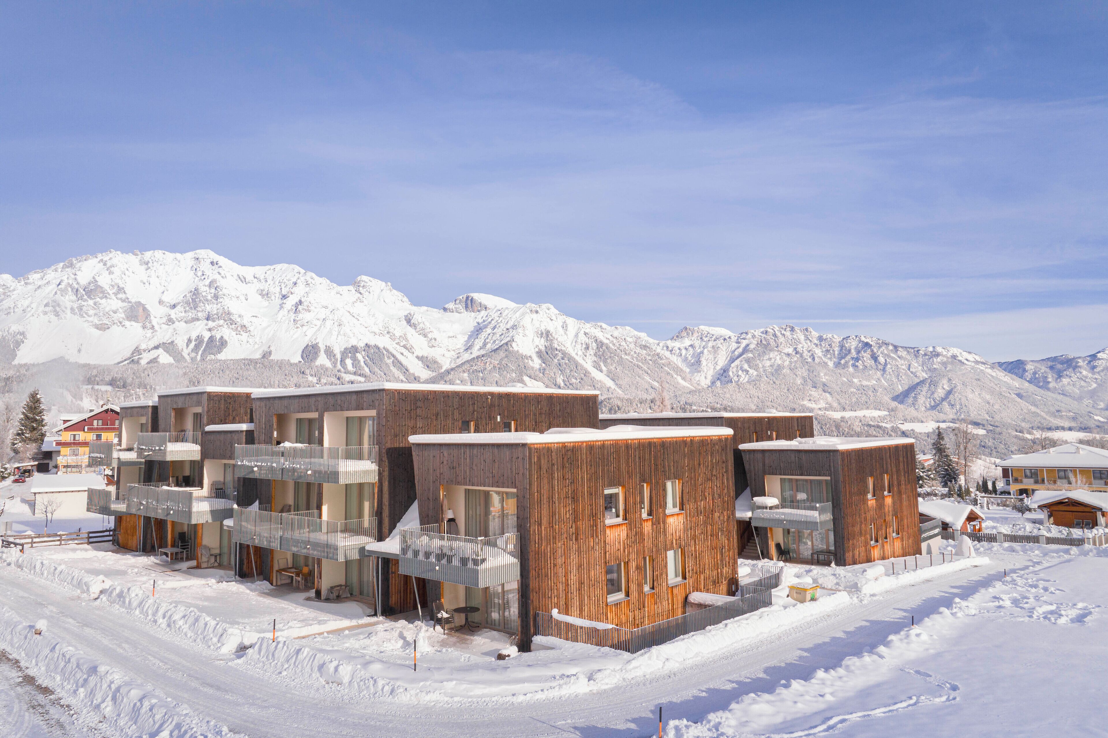 A modern building complex with multiple balconies and a snowy mountain backdrop.