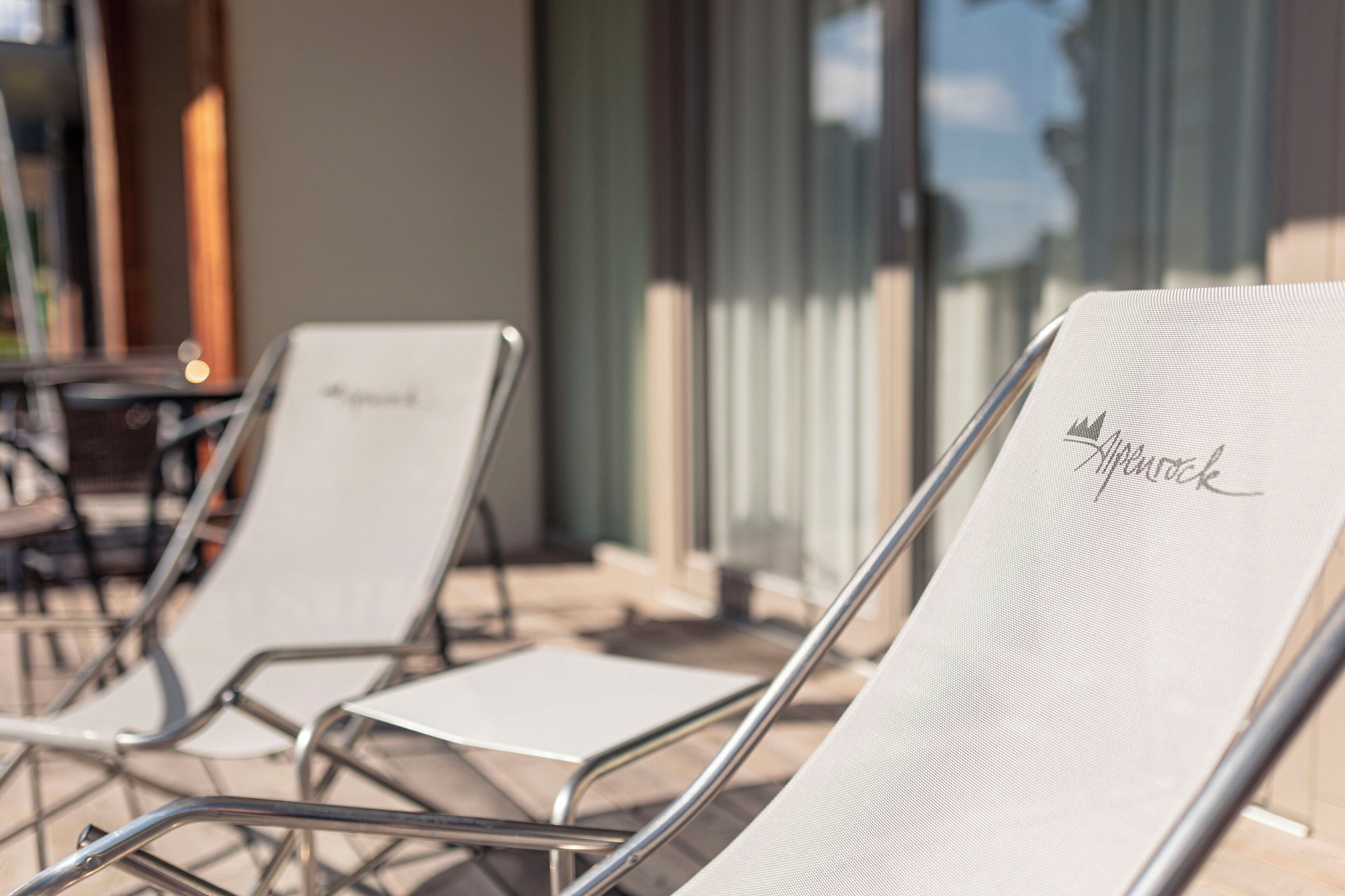 Deux fauteuils de relaxation dotés d’une structure en métal et de coussins blancs, placés sur une terrasse pourvue d’une balustrade en verre et offrant une vue sur le ciel.