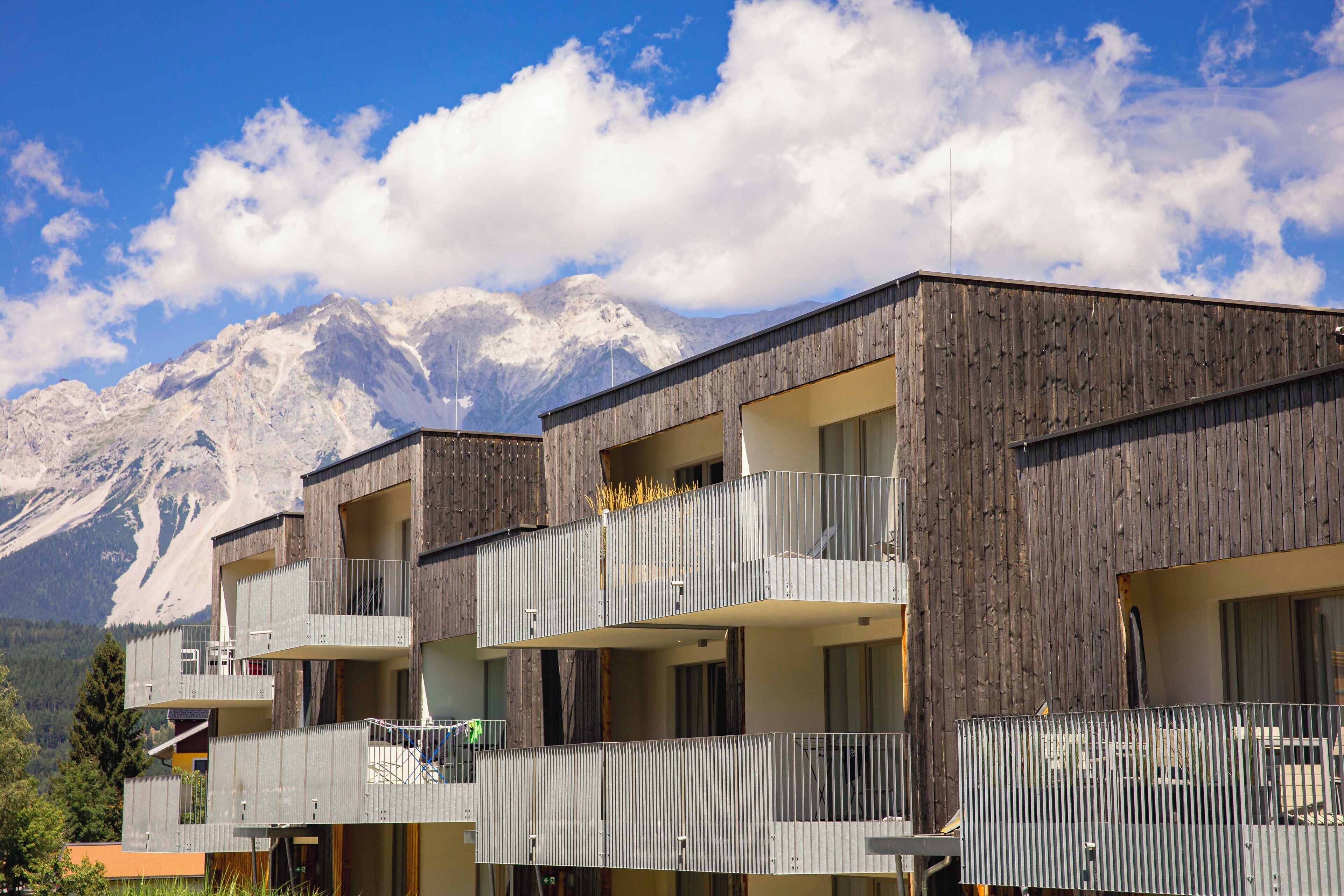 A modern building with multiple balconies and large windows, set against a backdrop of snow-capped mountains.
