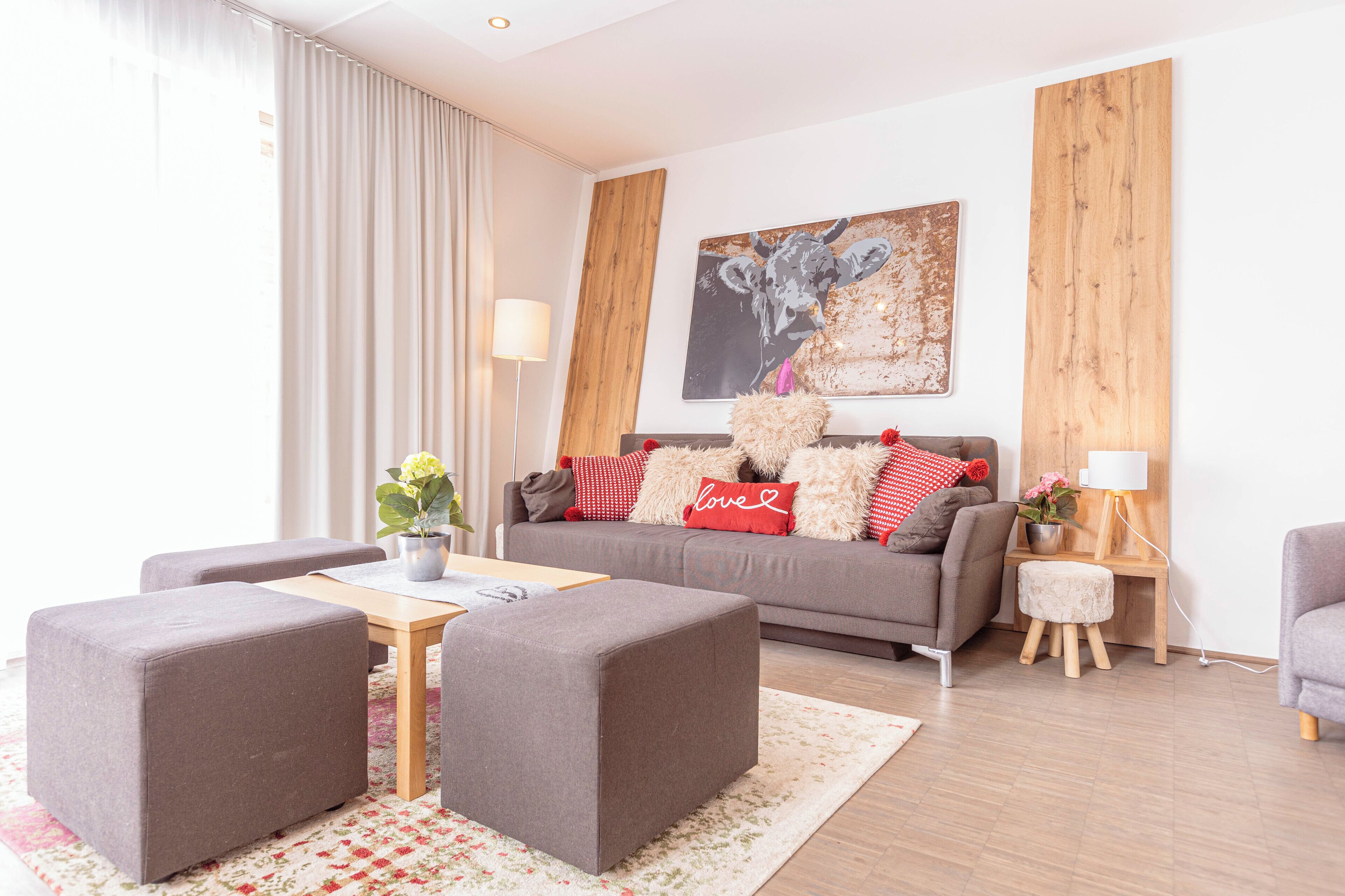 A modern living room with a grey sofa, two grey ottomans, a wooden coffee table, and a floral rug.