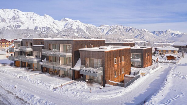 Un bâtiment moderne doté de nombreux balcons et de grandes fenêtres, entouré de montagnes enneigées.