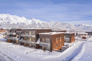 Un bâtiment moderne doté de nombreux balcons et de grandes fenêtres, entouré de montagnes enneigées.