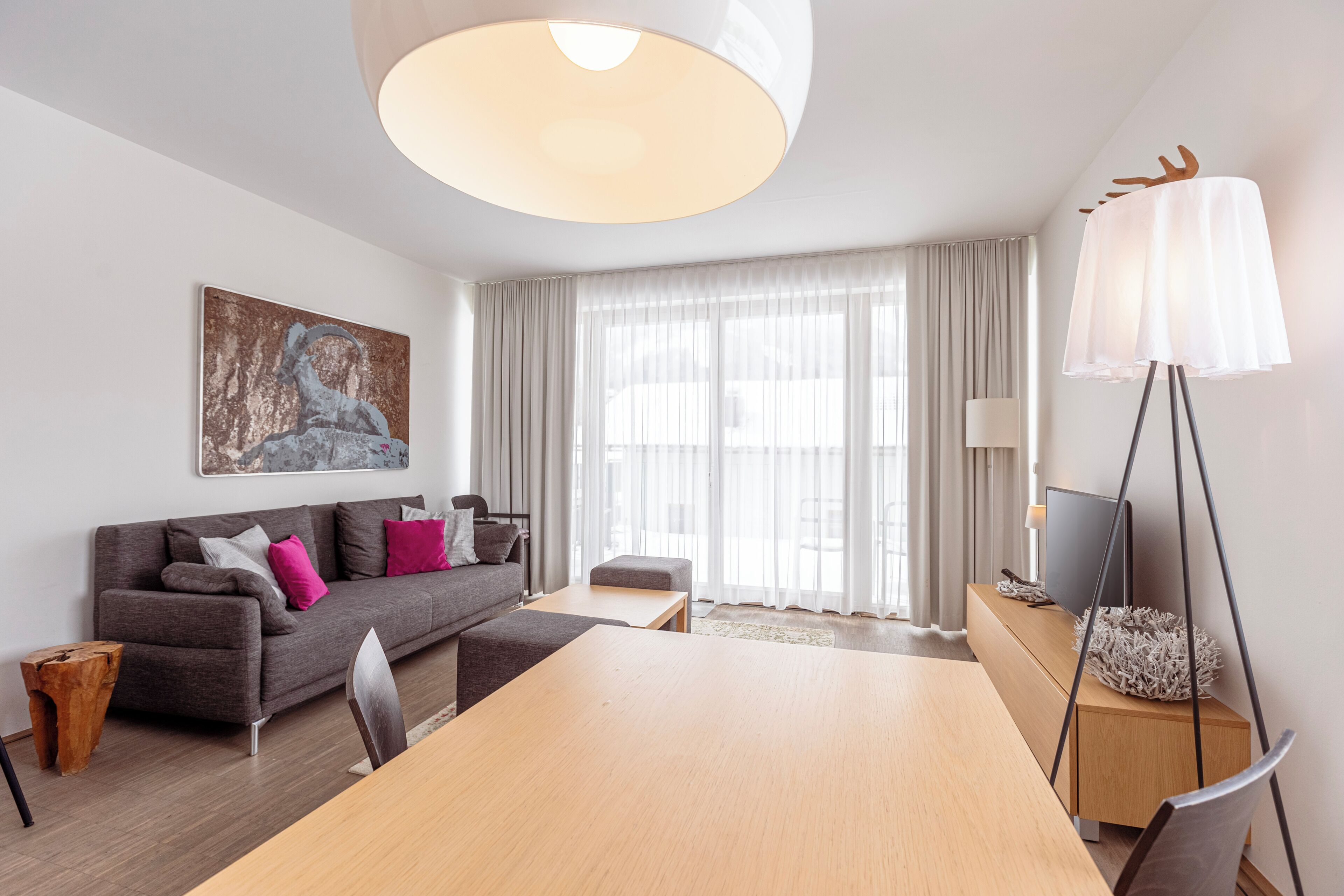A modern living room with a sofa, a dining table, a lamp, and a television.