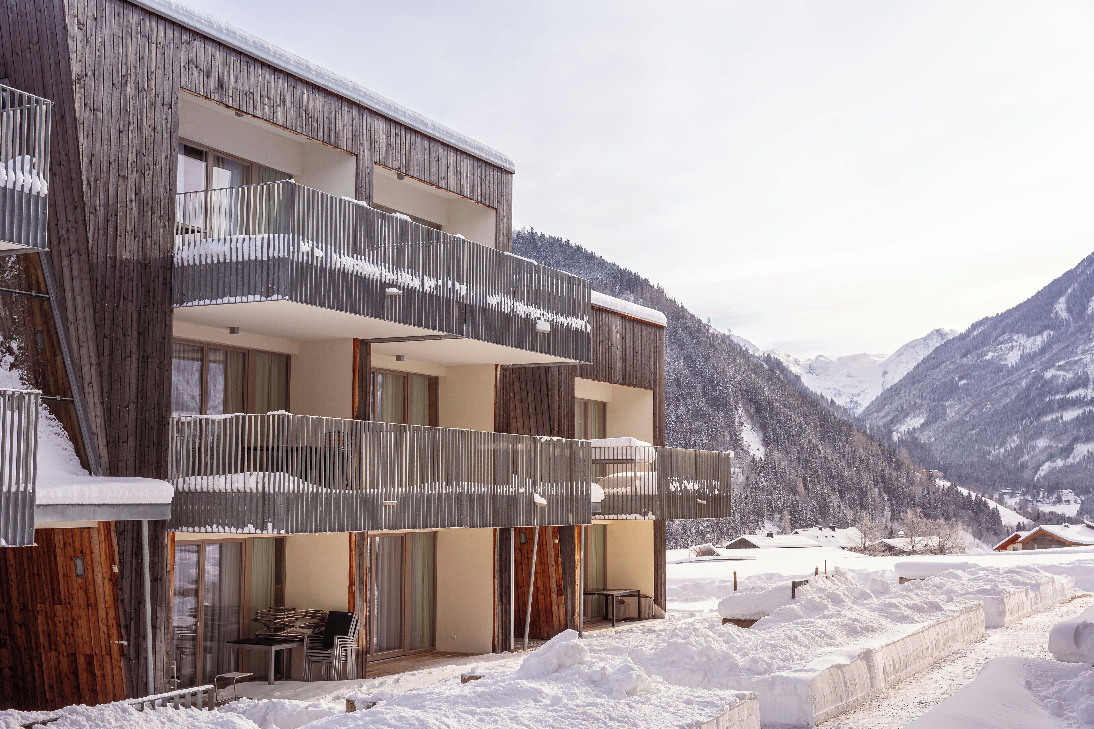Un edificio moderno a più piani con balconi, facciata in legno e uno sfondo montuoso innevato.