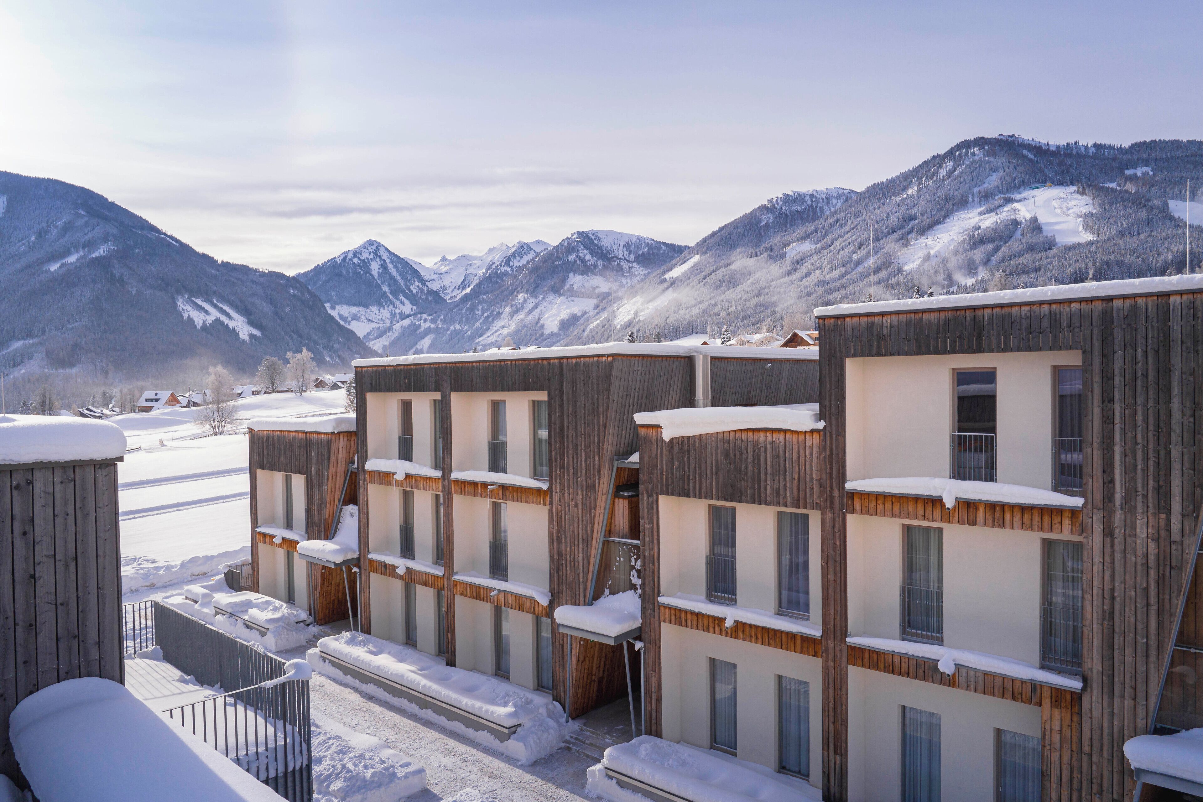Una hilera de edificios de madera con balcones, frente a un paisaje montañoso nevado.