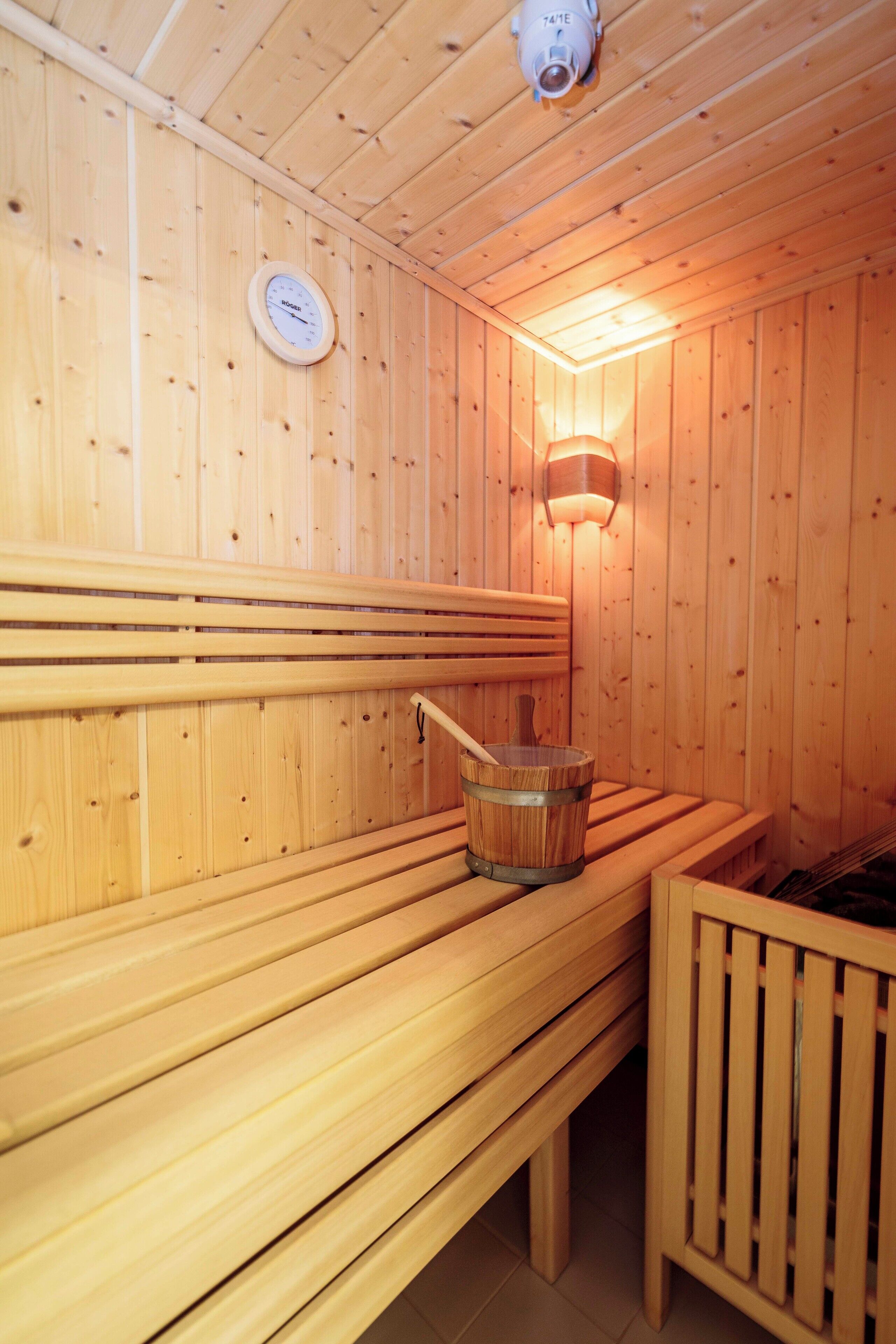 Un sauna en bois avec des bancs, une horloge fixée au mur et un luminaire de sauna.