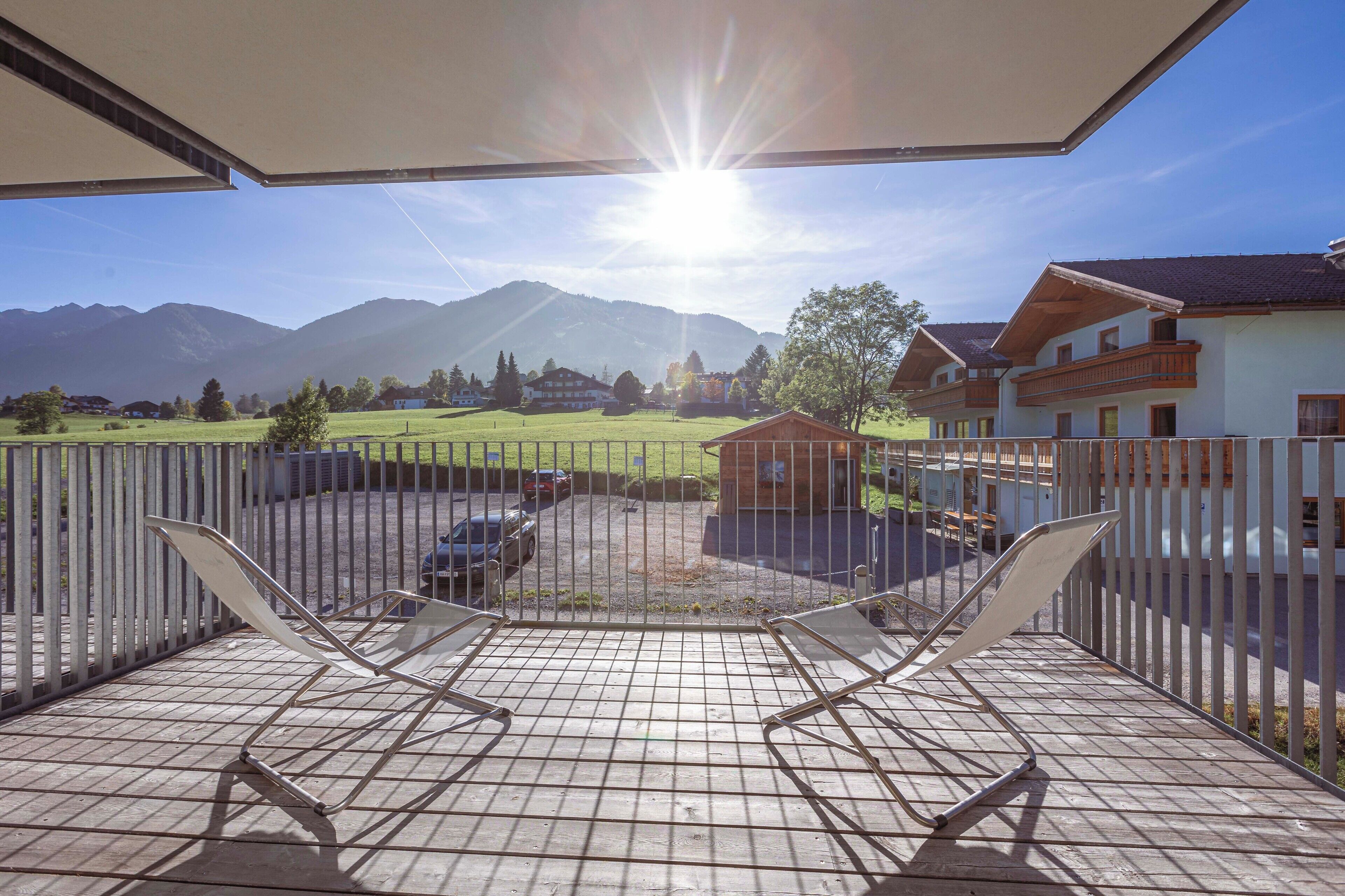 A balcony with metal chairs, a view of a mountain, and a building with a balcony.