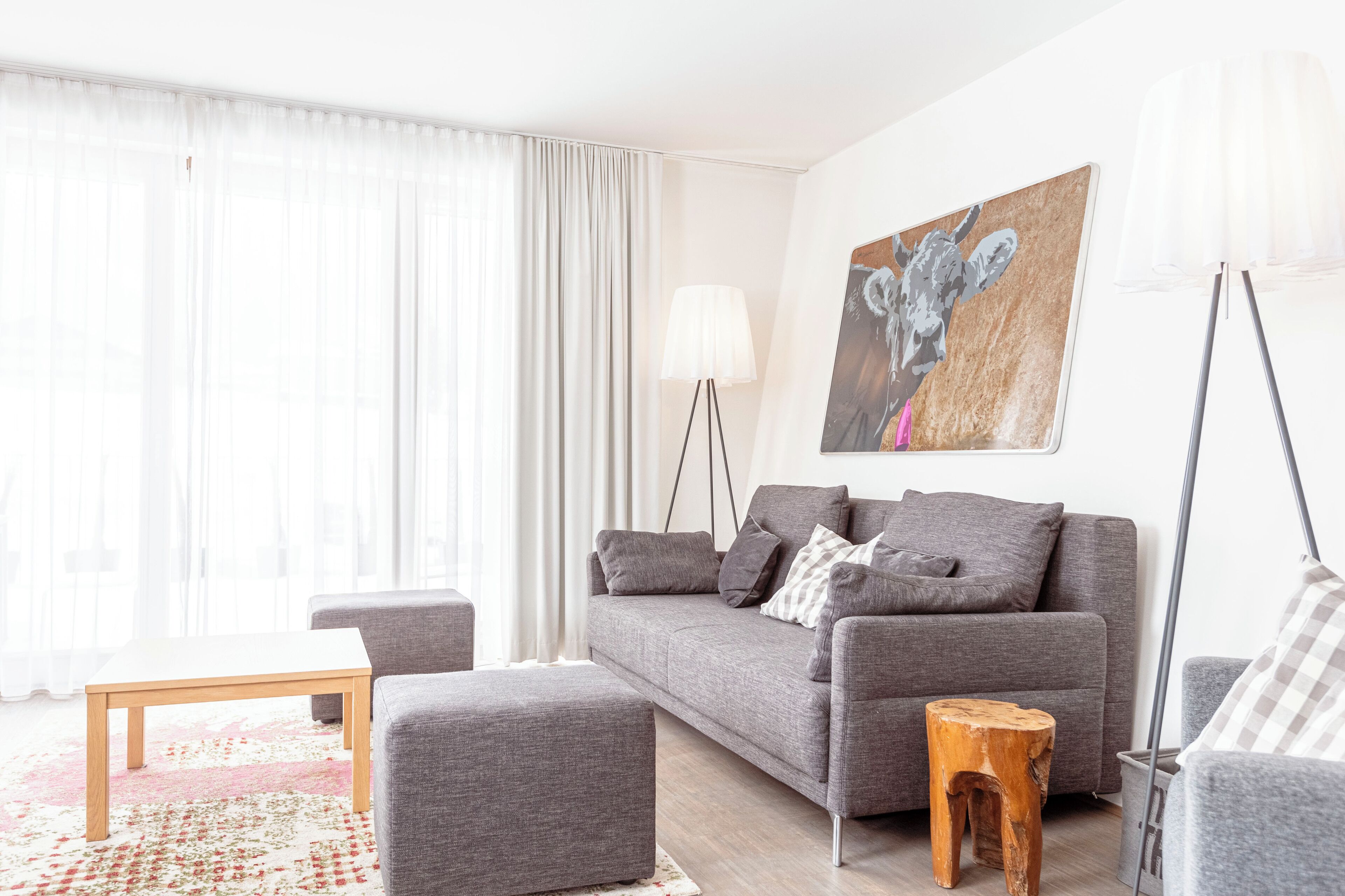 A modern living room with a grey sofa, a wooden coffee table, and a small wooden stool.