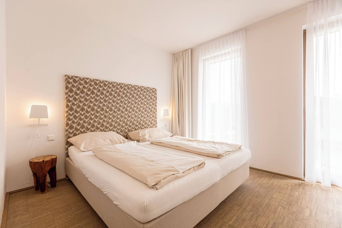 Een tweepersoonsbed met een gestreept hoofdbord, twee bedlampjes en een houten nachtkastje.