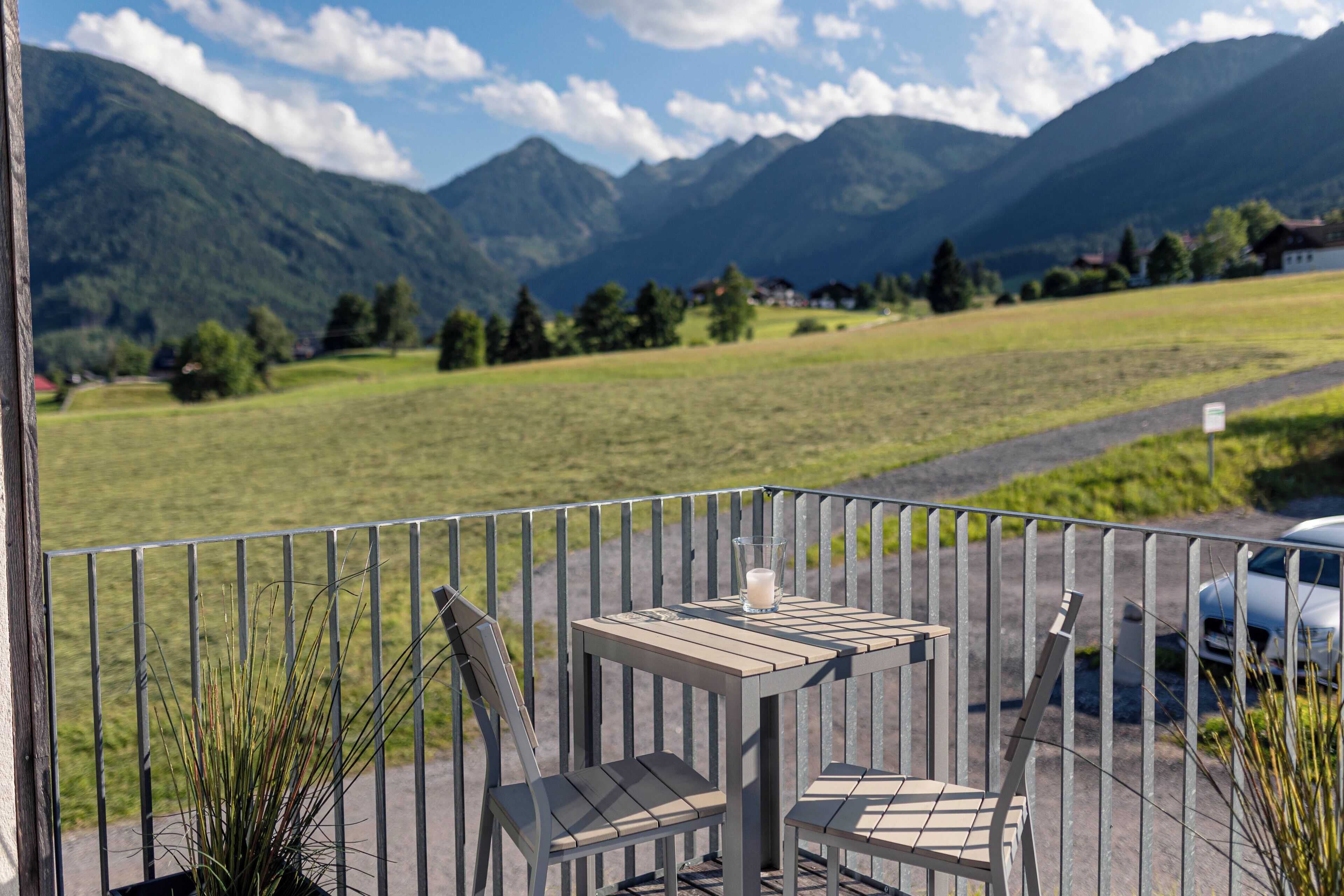 A balcony with a table and chairs, overlooking a mountainous landscape.
