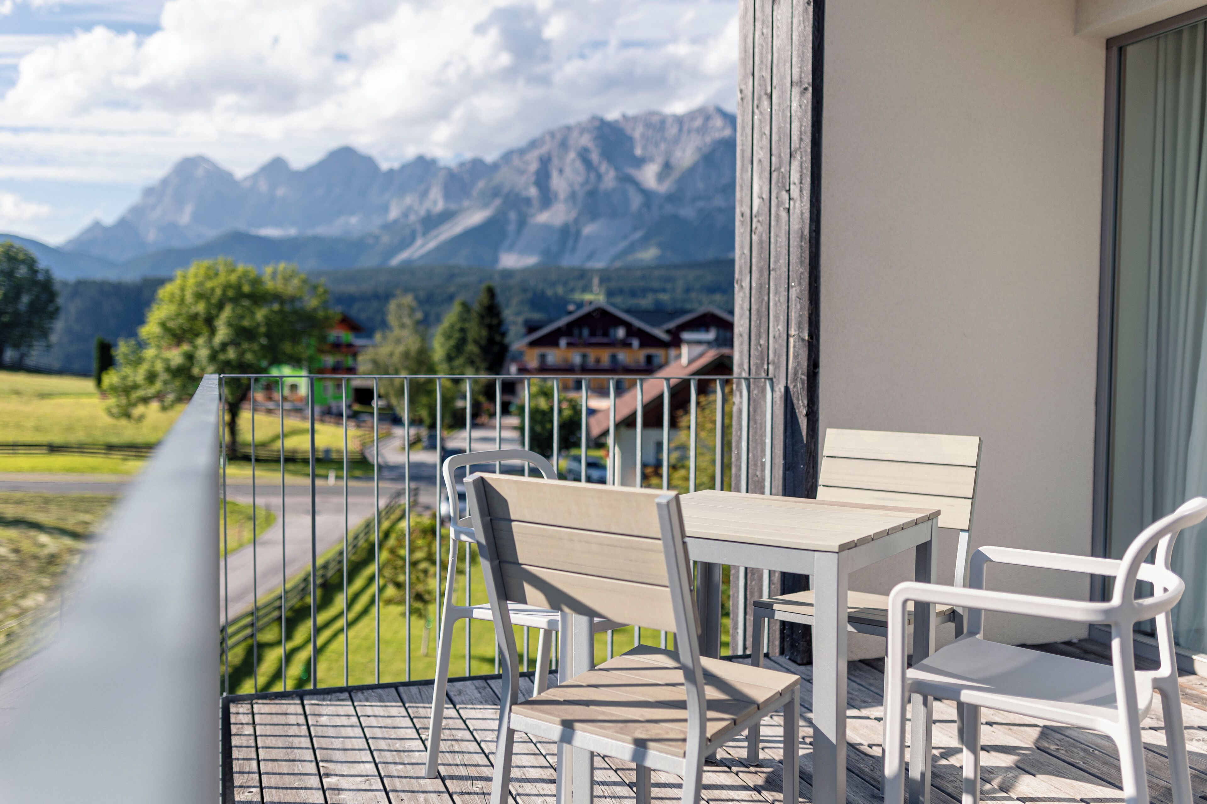 Een balkon met een tafel en stoelen, met uitzicht op een berglandschap met huizen op de achtergrond.