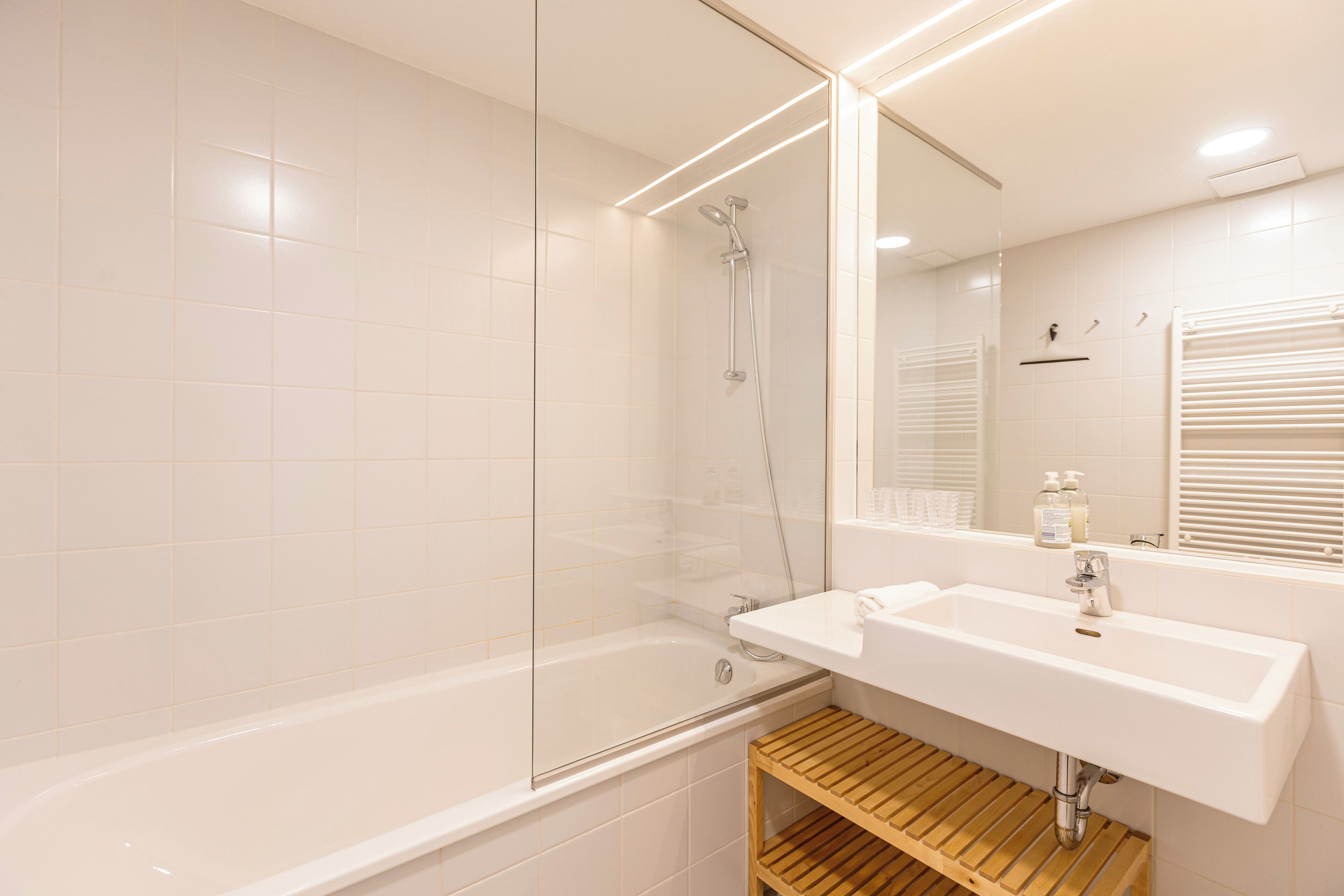 Een moderne badkamer met een douche met glazen wand, een wit wastafelmeubel en een houten plank.
