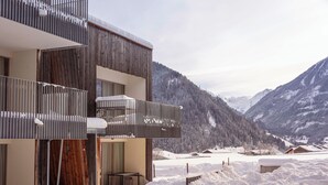Un bâtiment moderne doté d’une façade en bois, de balcons et offrant une vue sur des montagnes enneigées.