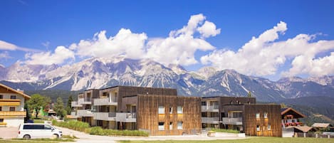 Un bâtiment moderne doté de nombreux balcons, d’un espace de stationnement et d’un terrain herbeux à l’avant.