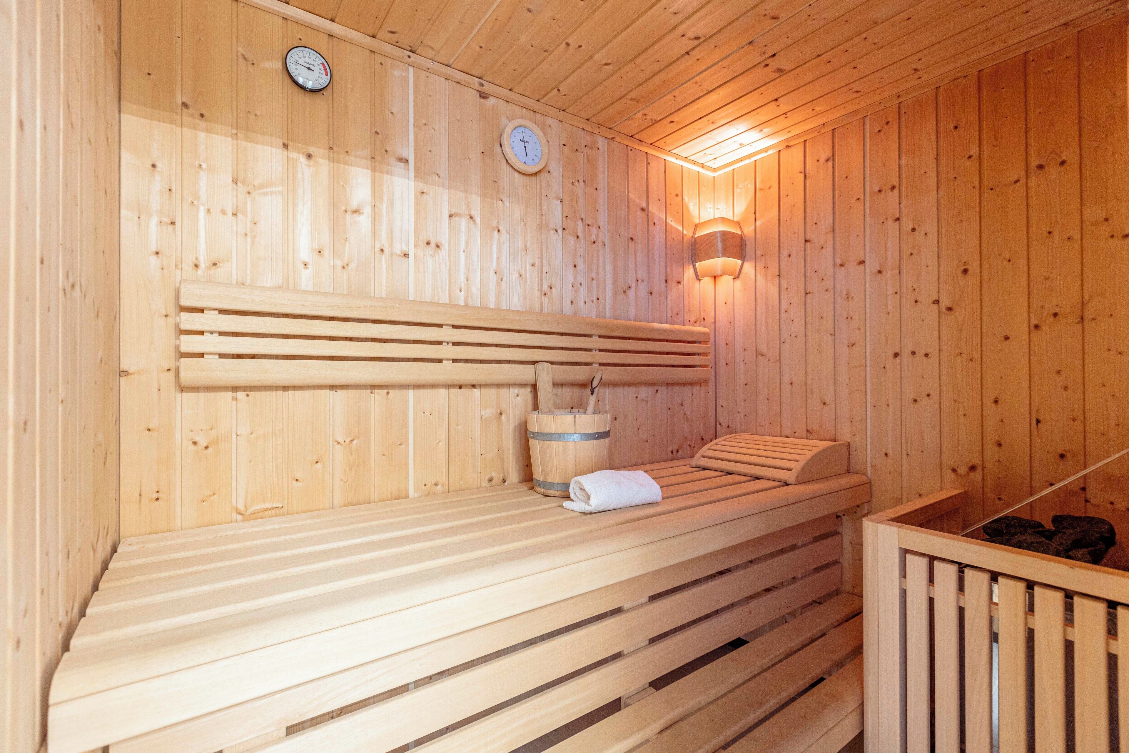 A wooden sauna with benches, a clock, and a wall-mounted light fixture.