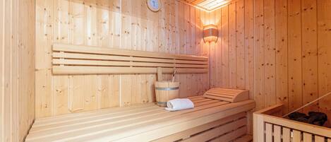 A wooden sauna with benches, a clock, and a wall-mounted light fixture.