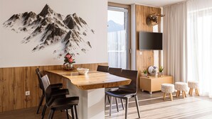 Un espace repas moderne avec une table et des chaises en bois, un téléviseur fixé au mur et une fresque représentant une montagne sur le mur.