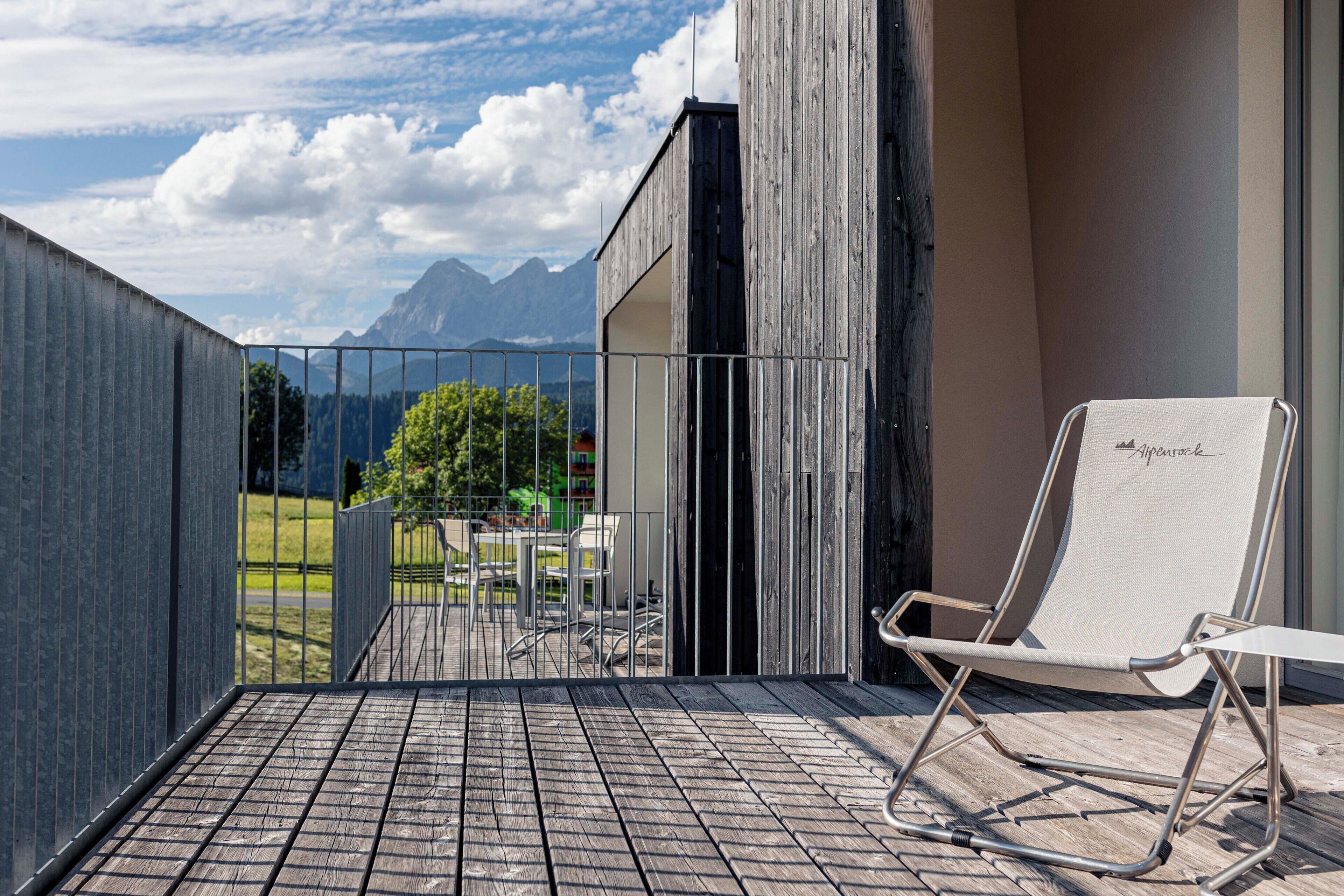 A balcony with a metal railing, a white lounge chair, and a view of mountains and greenery.