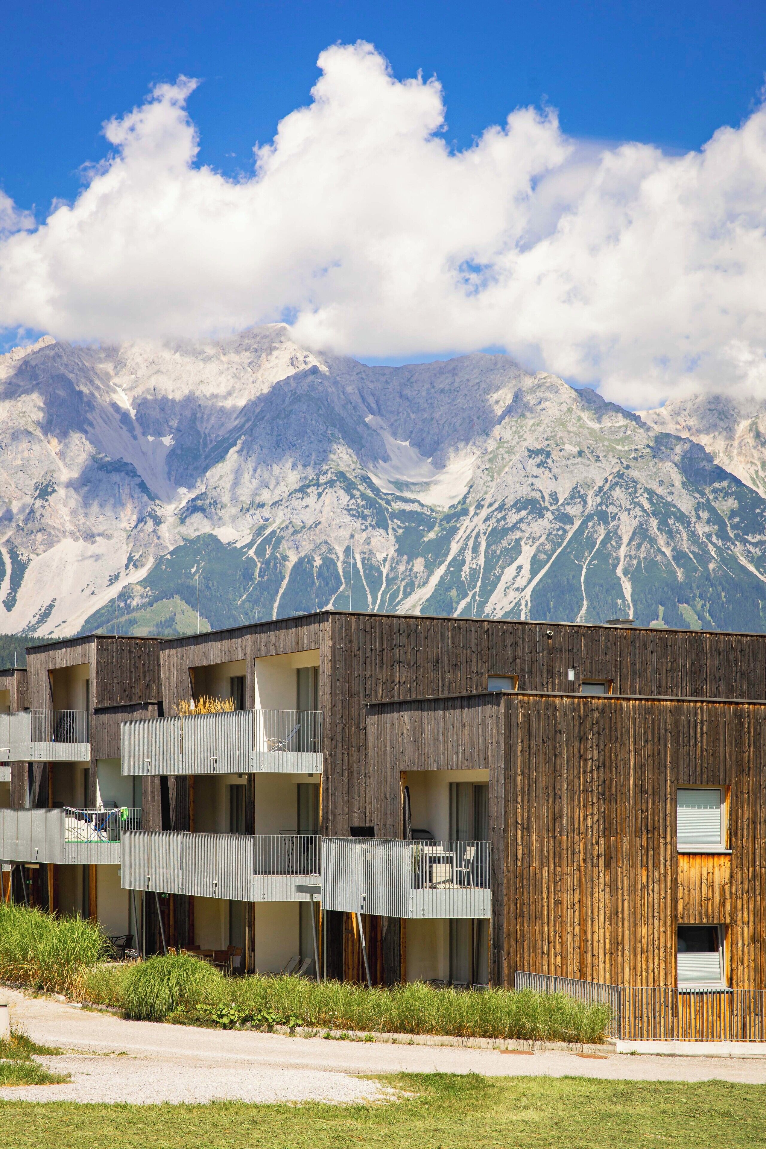 A modern building with multiple balconies, wooden facade, and a view of snow-capped mountains.