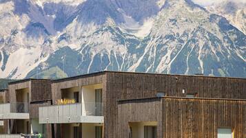 A modern building with multiple balconies, wooden facade, and a view of snow-capped mountains.