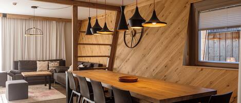 Un comedor moderno con una mesa y sillas de madera, luces colgantes y un amplio ventanal con persianas.