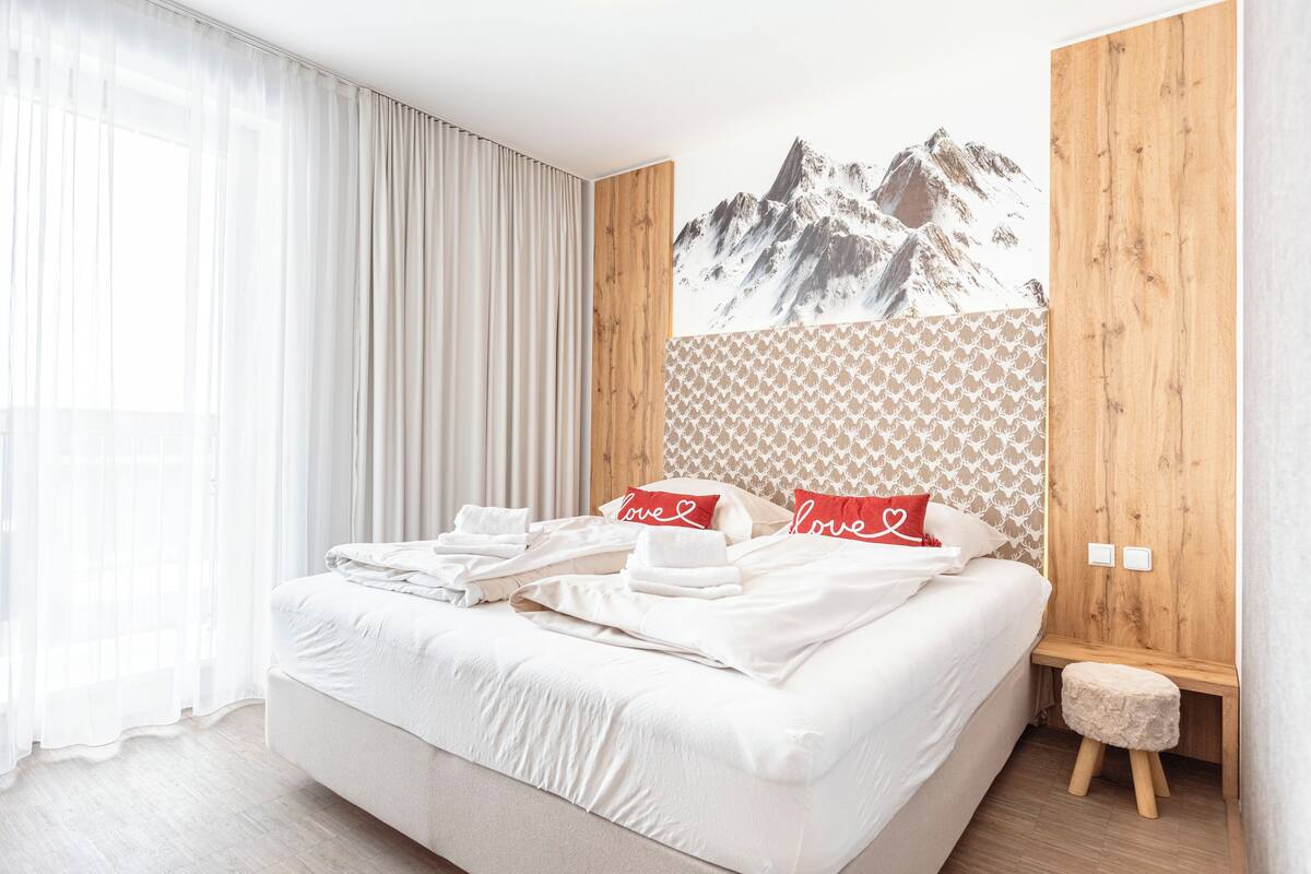 Een keurig opgemaakt bed met witte lakens en een muurschildering van een berglandschap.