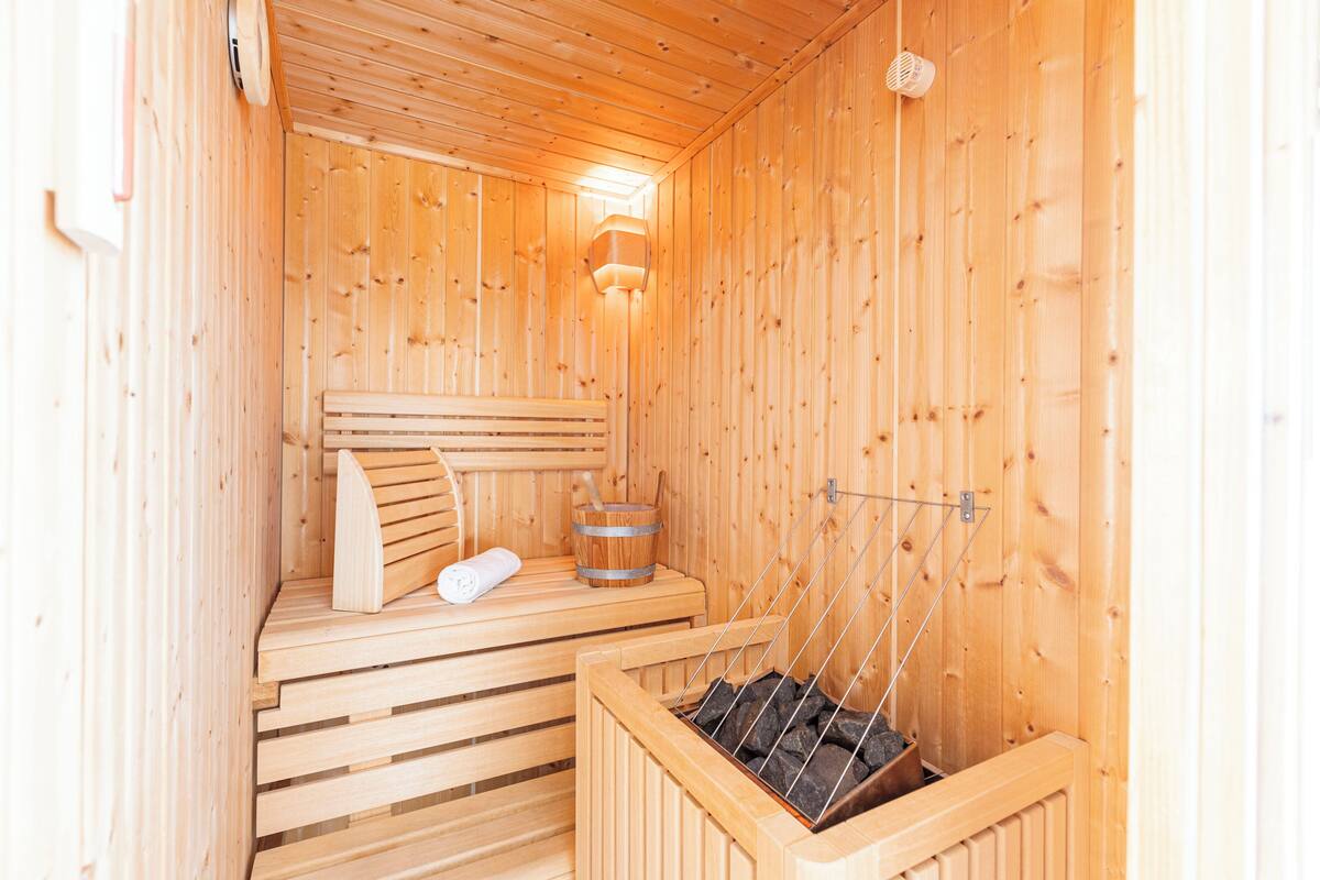 Een houten sauna met banken, een verwarmde vloer en een emmer stenen.
