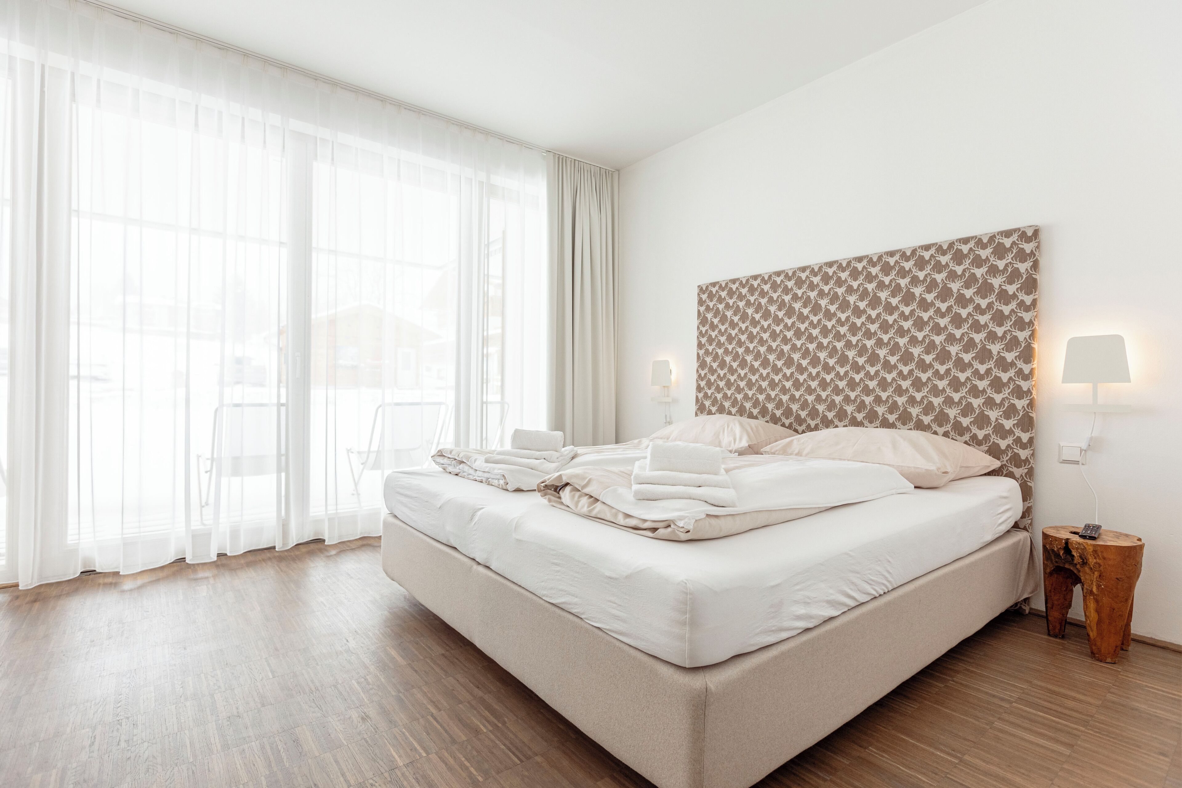 Una cama bien tendida con sábanas blancas, un cabecero de madera con diseño decorativo y una mesita de noche con una lámpara.