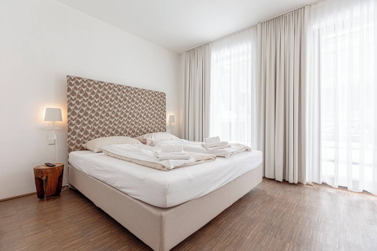 Een net opgemaakt bed met witte lakens, een gestreept hoofdbord en twee bedlampjes.