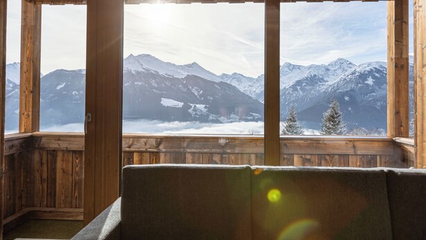 Eine Holzdiele mit großen Fenstern, die einen Blick auf schneebedeckte Berge bietet.