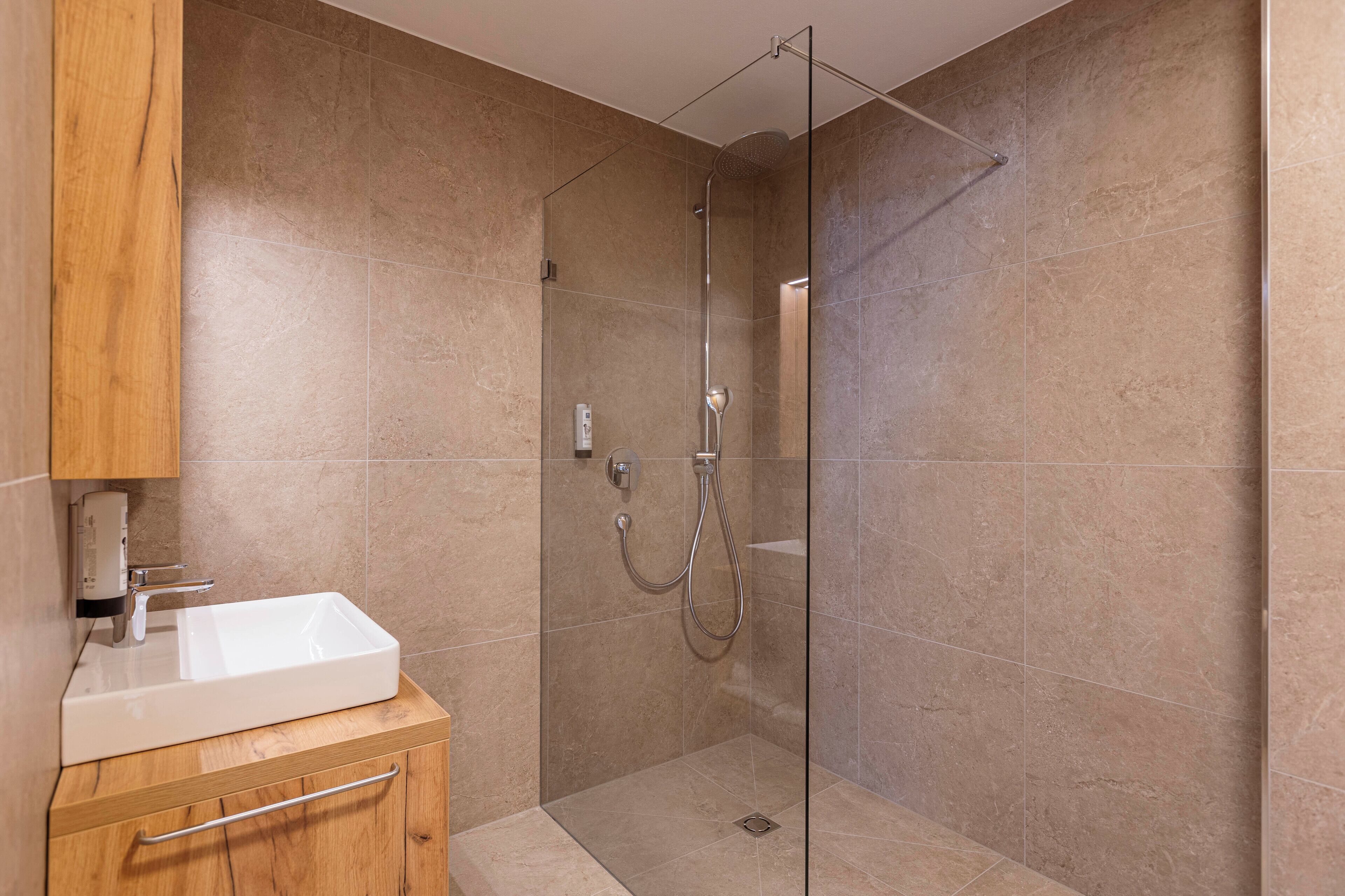 A modern bathroom with a glass-enclosed shower, a wooden vanity with a sink, and a mirror.