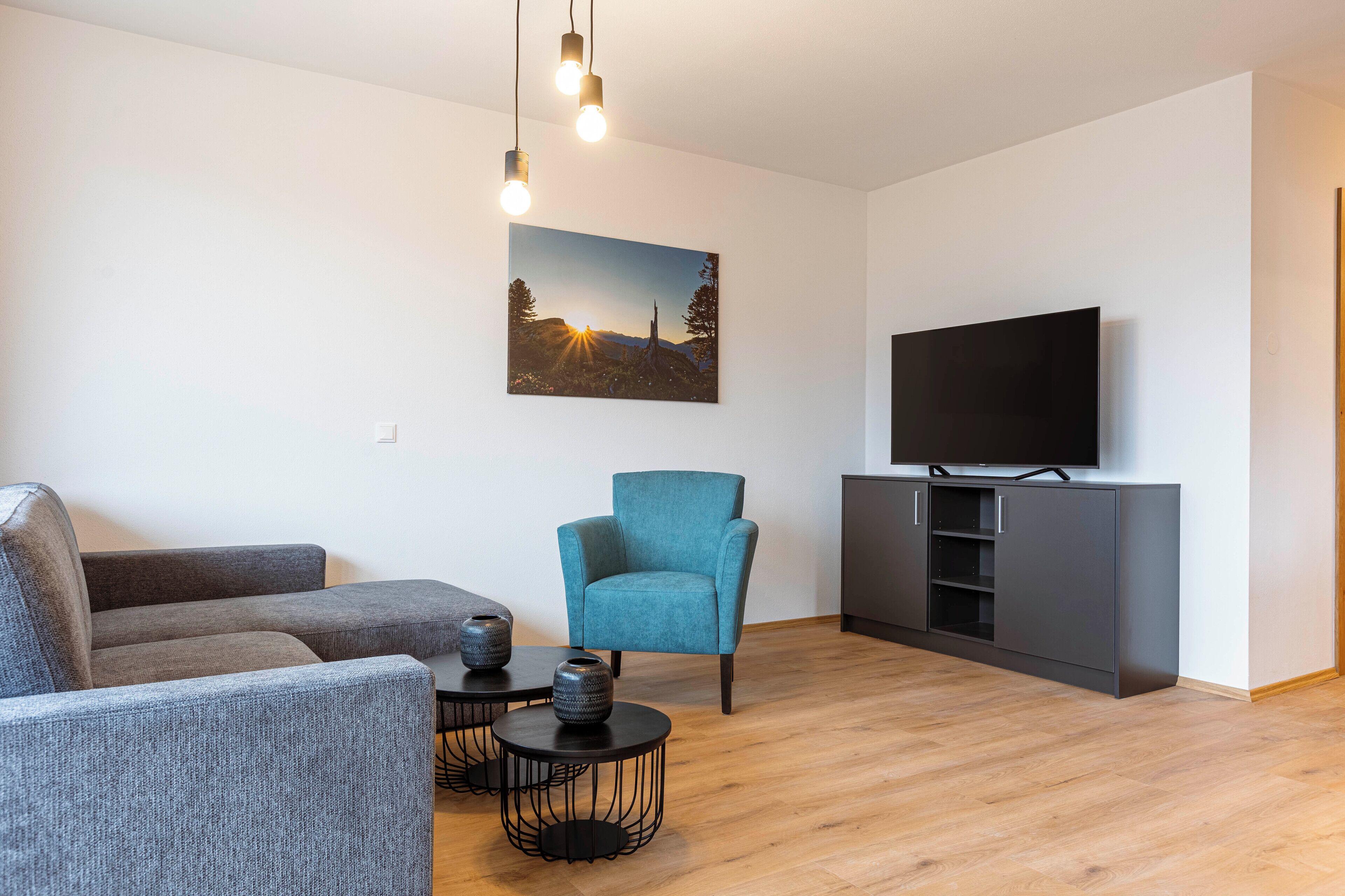 Ein modernes Wohnzimmer mit grauem Sofa, blauem Sessel, Flachbildfernseher und Schrank.