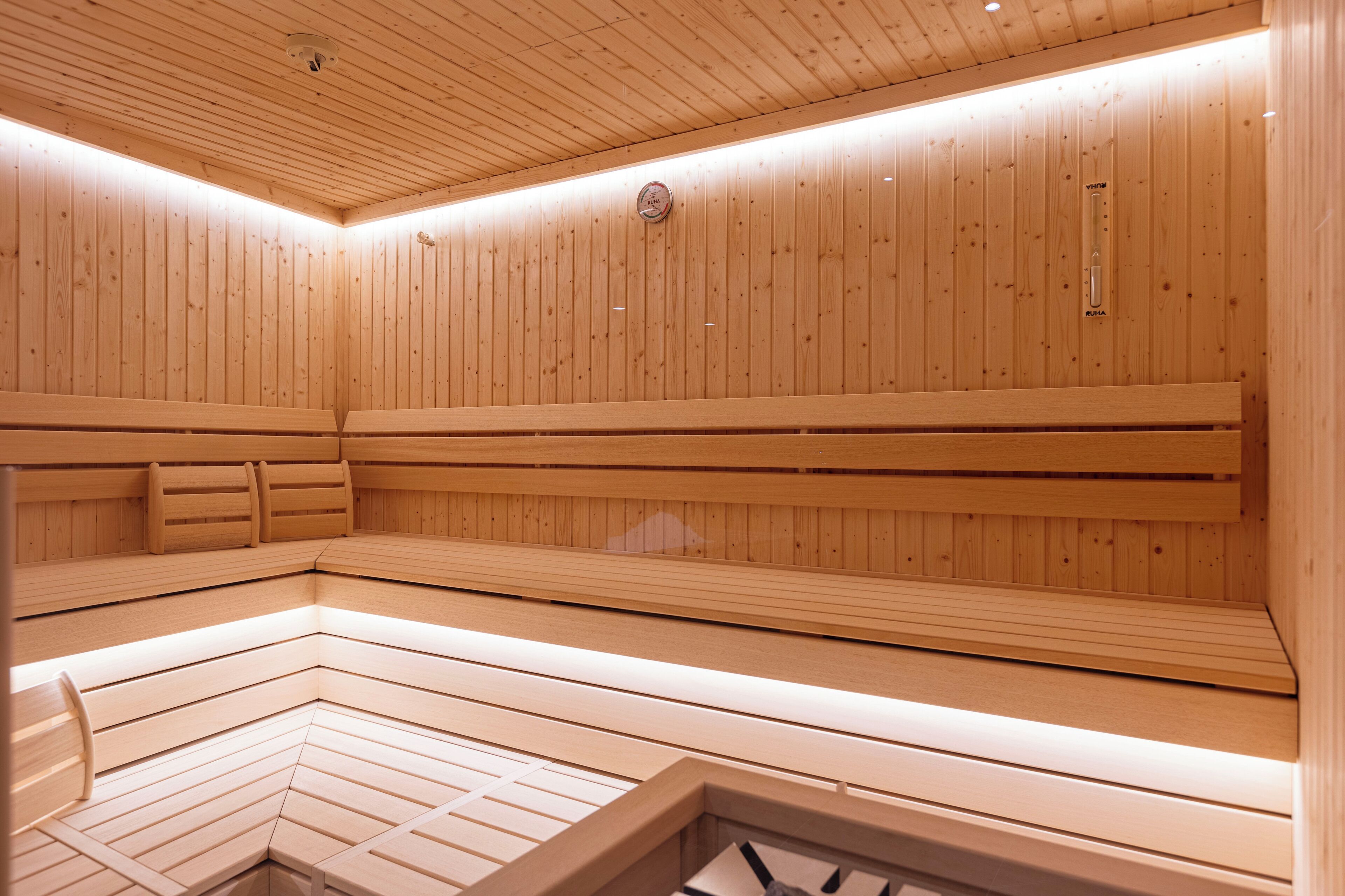 Un sauna avec des bancs en bois et un plancher incliné, des murs en bois et un plafond doté d’un éclairage encastré.