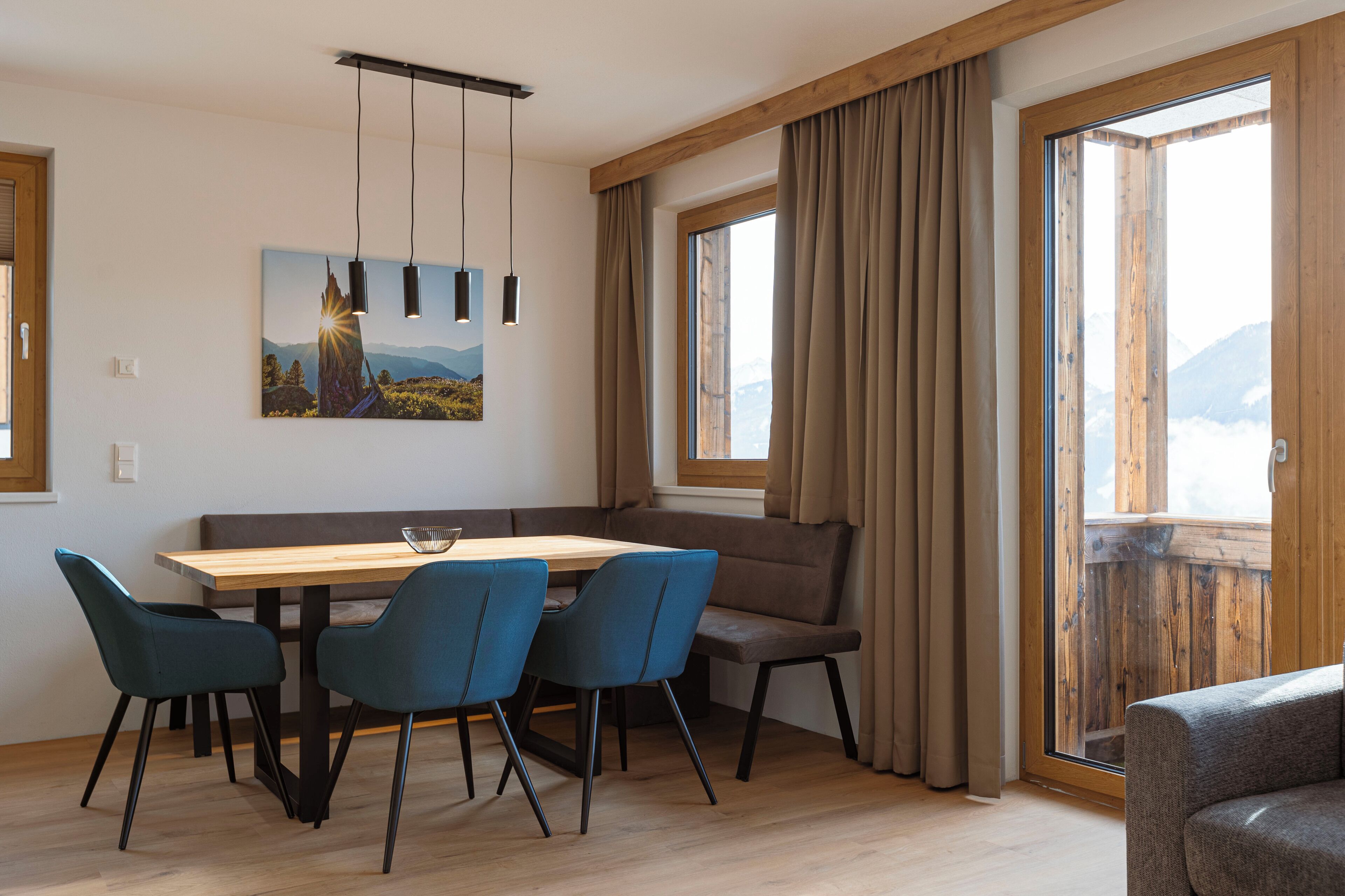 A dining area with a wooden table, four blue chairs, a bench, and a painting of a mountain scene.