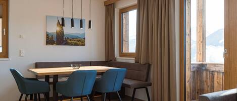 A dining area with a wooden table, four blue chairs, a bench, and a painting of a mountain scene.