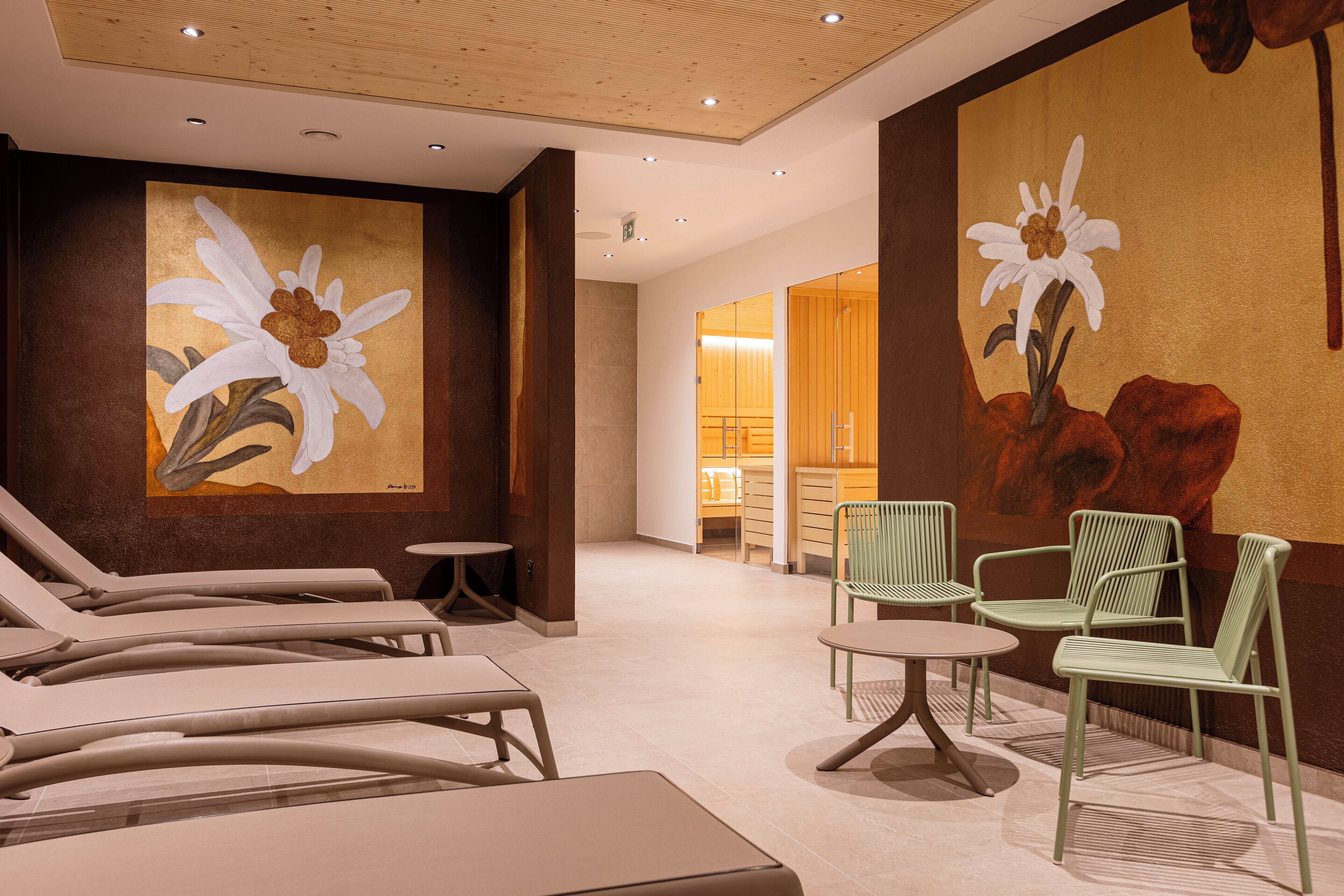 A spa area with lounge chairs and a table, a large floral mural on the wall, and a wooden ceiling.