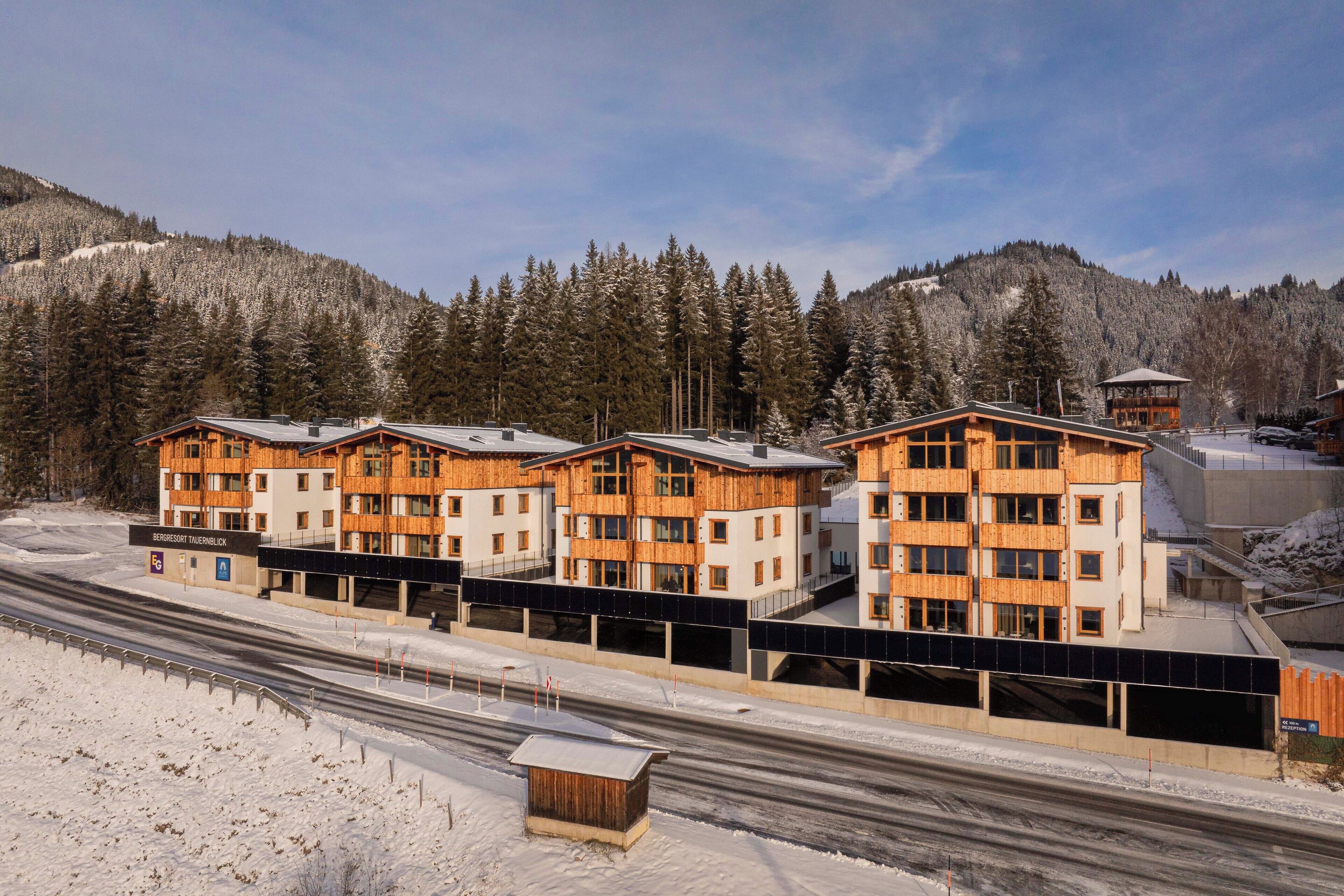 Ett modernt hotell med flera byggnader som har trästomme, en parkeringsplats och en snötäckt bergskedja i bakgrunden.