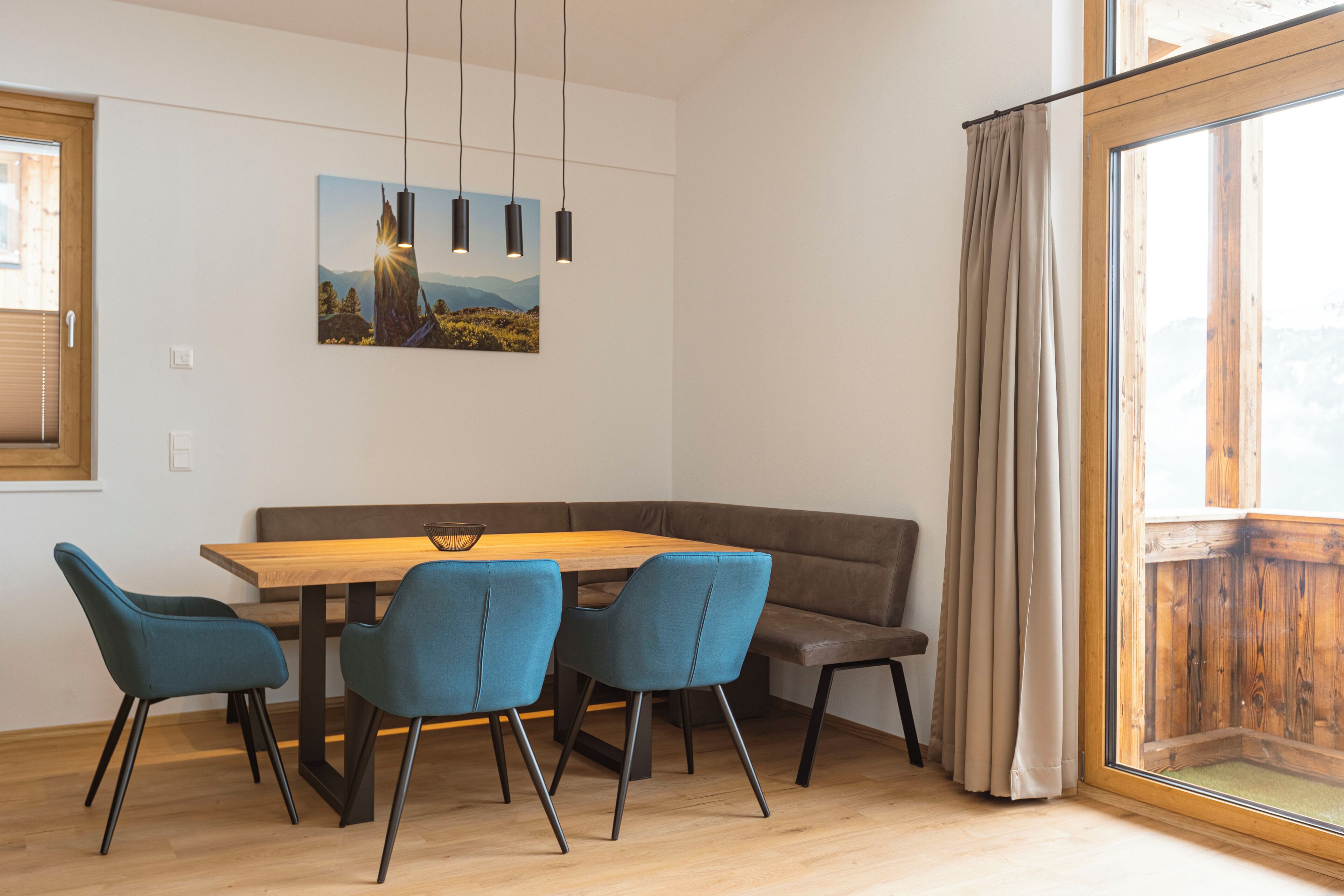 Un coin repas avec une table en bois et quatre chaises bleues, un canapé marron et un tableau accroché au mur.