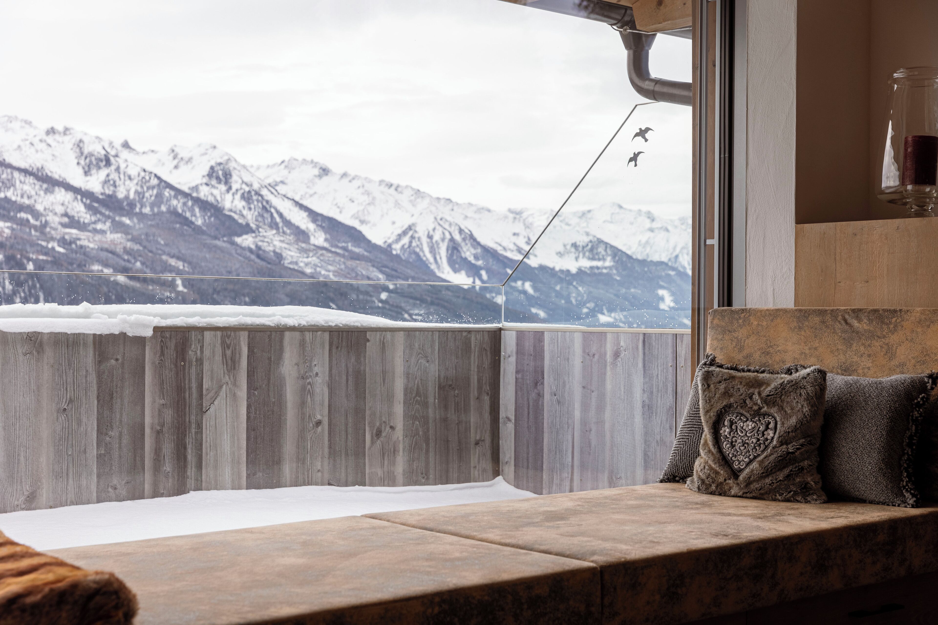 A wooden bench with a view of snow-covered mountains through a window.