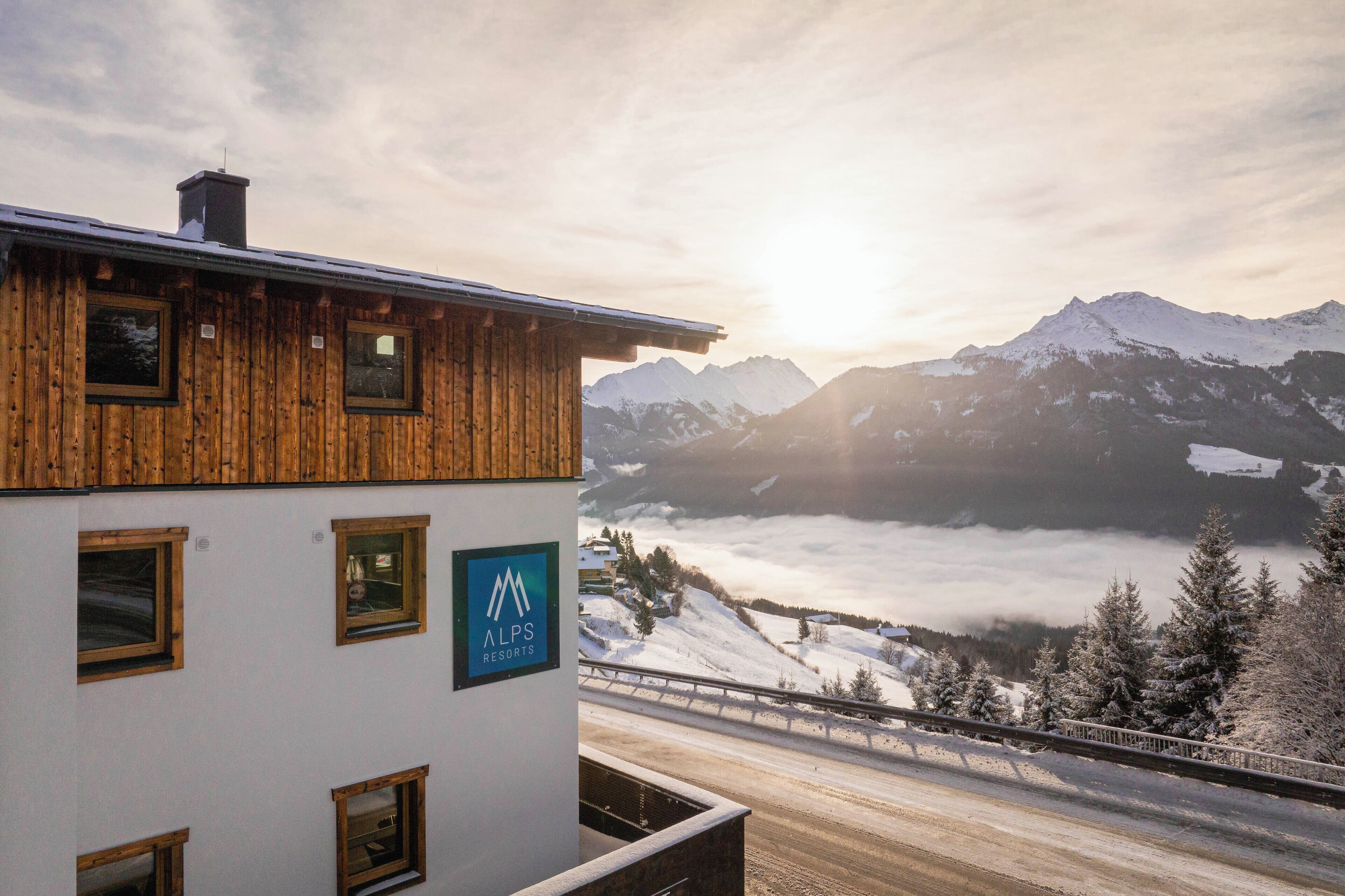 A wooden building with a sign for ALPS Resorts, overlooking a snow-covered mountain range and a valley.