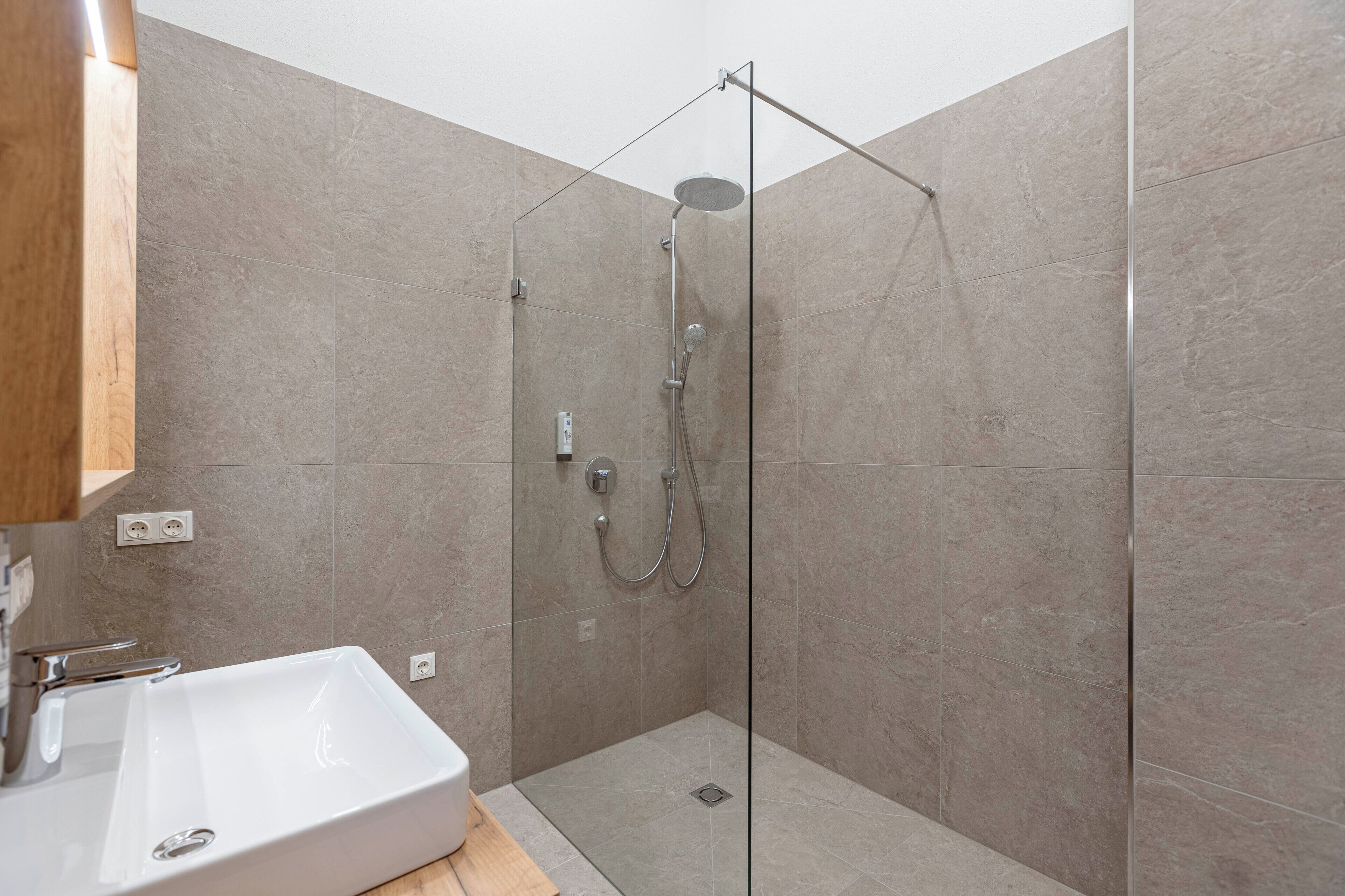 Une salle de bain moderne avec une douche à parois de verre, un lavabo blanc et un meuble-lavabo en bois.