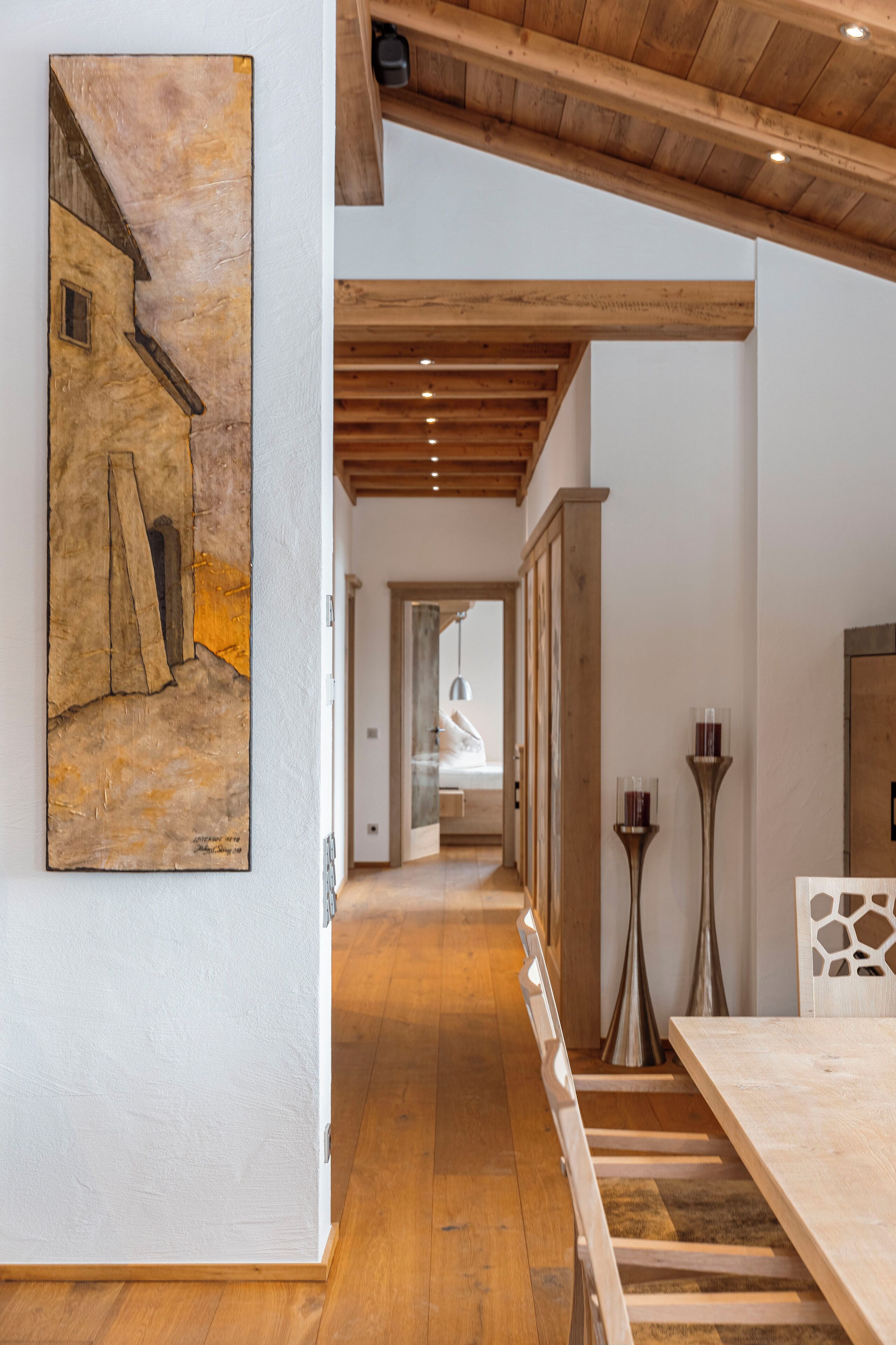 Un pasillo con suelo de madera, un comedor con una larga mesa y un cuadro en la pared.