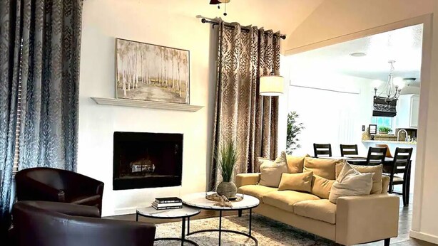 A living room with a sofa, two coffee tables, a fireplace, and a dining area visible through an open doorway. - Amistad House (Del Rio)