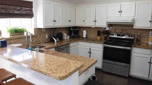 A kitchen with white cabinets, granite countertops, a stainless steel stove, and a coffee maker. - Amistad House (Del Rio)
