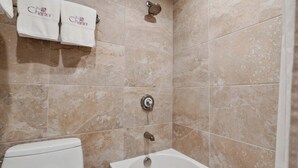 A bathroom with beige marble tiles, a white bathtub, and a toilet. There are two towels hanging on the wall with the text "The Charter".
