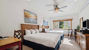 A hotel room with two beds, a desk, a television, and a ceiling fan.
